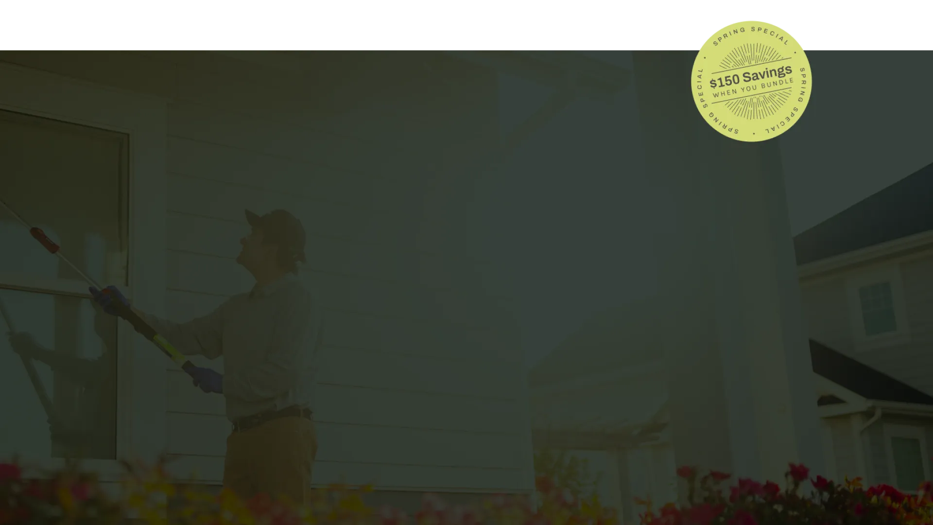 Man cleaning house window with long-handled brush outside on sunny day with flowers in foreground