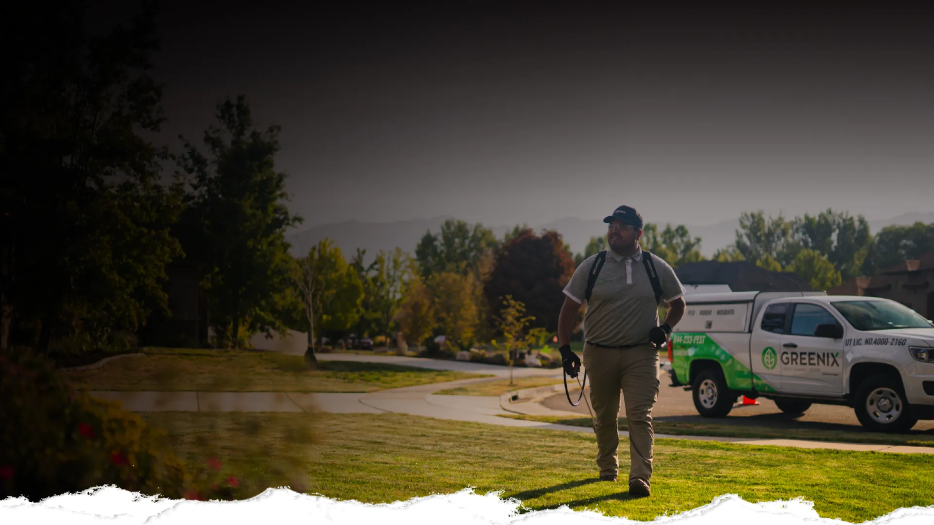 Landscaping worker walking on green lawn near Greenix service truck in suburban neighborhood on sunny day
