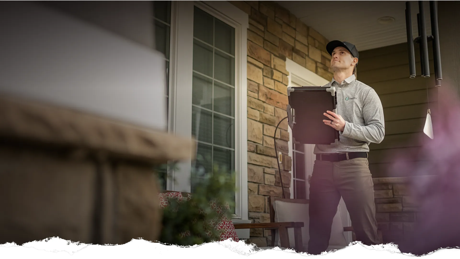 Home inspector in uniform evaluating a house exterior with tablet on a residential porch.