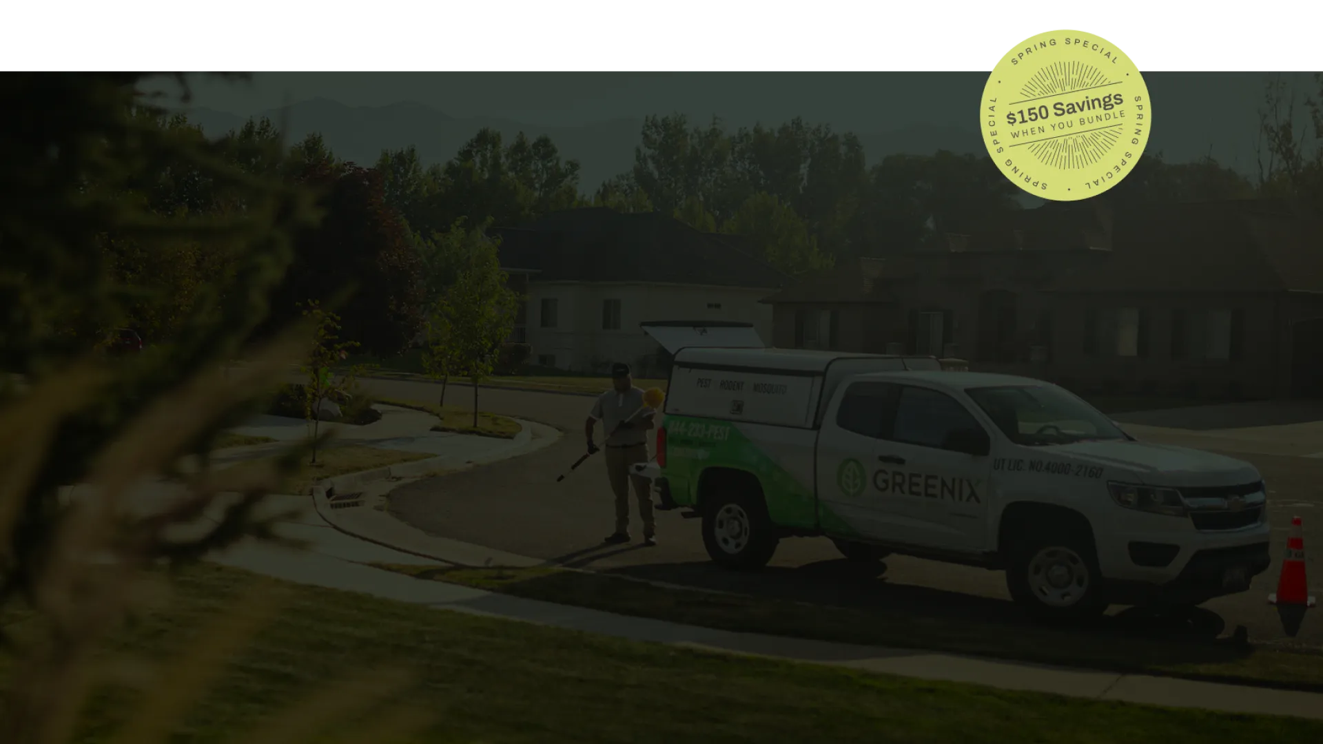 Landscaper working in a sunny residential neighborhood with Greenix service truck parked nearby and safety cone.