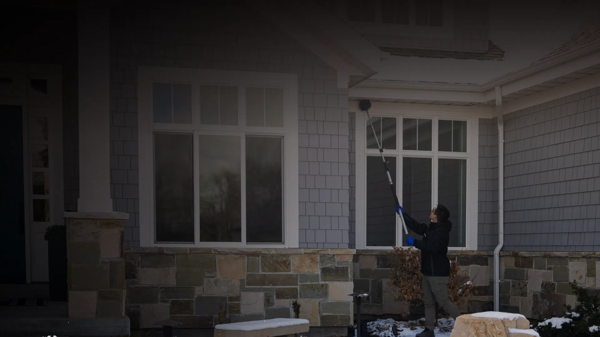 Person cleaning windows of a stone and shingles house during winter with snow on the ground