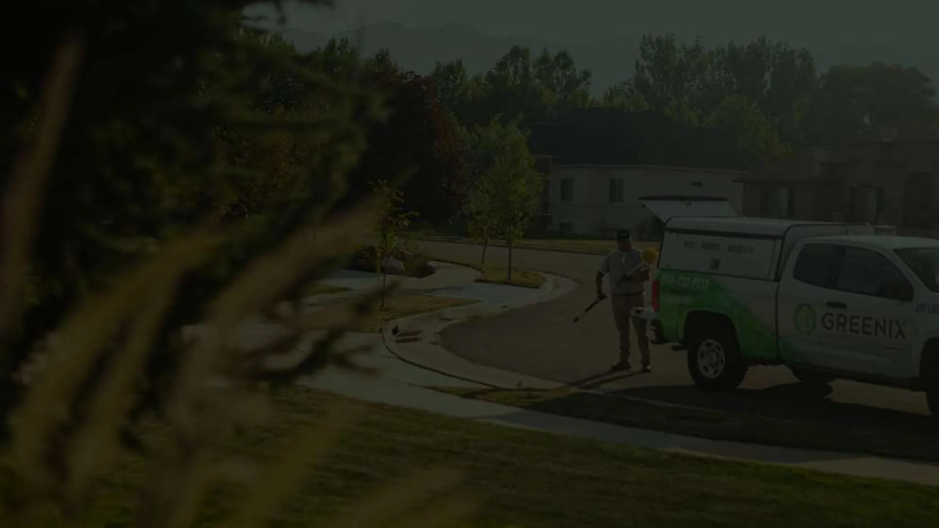 Landscaping worker using blowers beside a Greenix service truck on a suburban street during daytime.