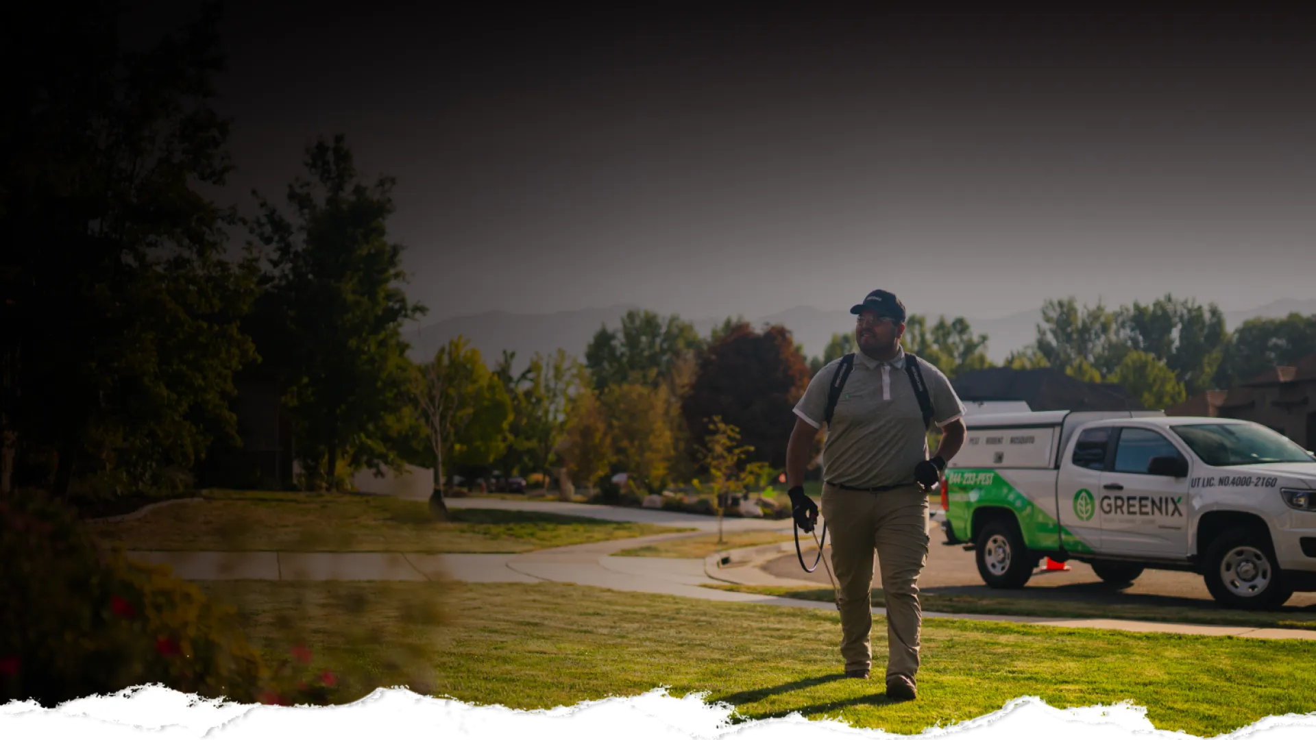 Lawn care professional walking on grass near a Greenix branded truck in a suburban neighborhood.