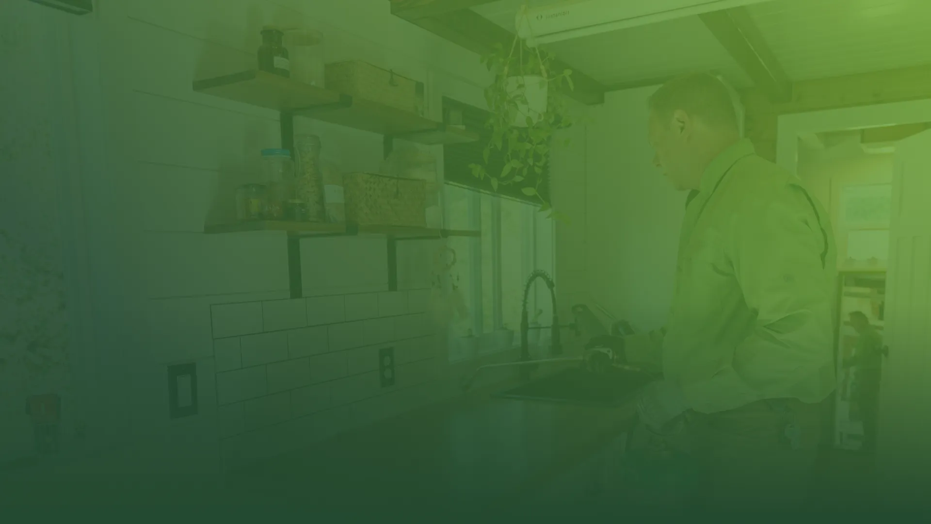 Man inspecting kitchen faucet and countertop with organized shelves and hanging plants in a modern kitchen
