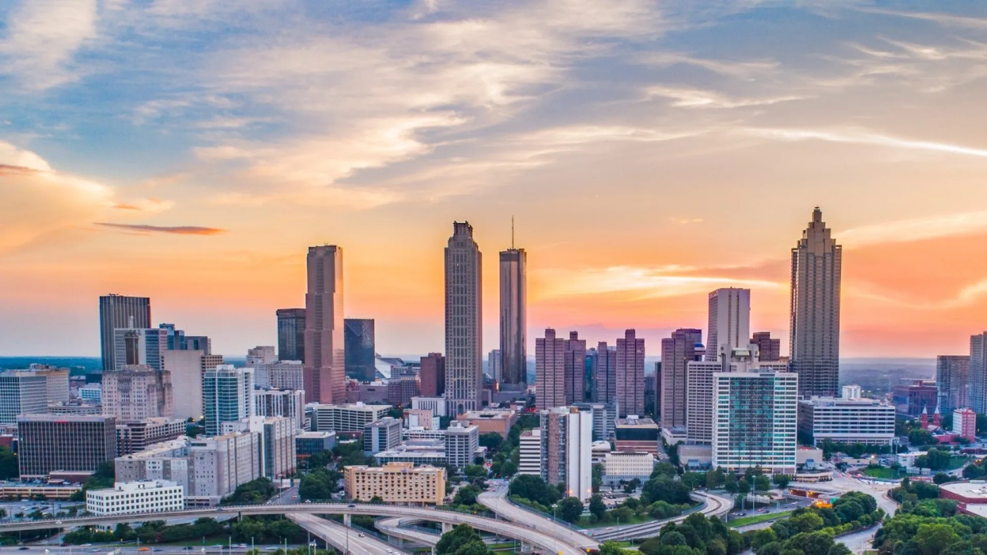 Sunset over Atlanta skyline with highways, residential areas, and skyscrapers under a colorful sky.