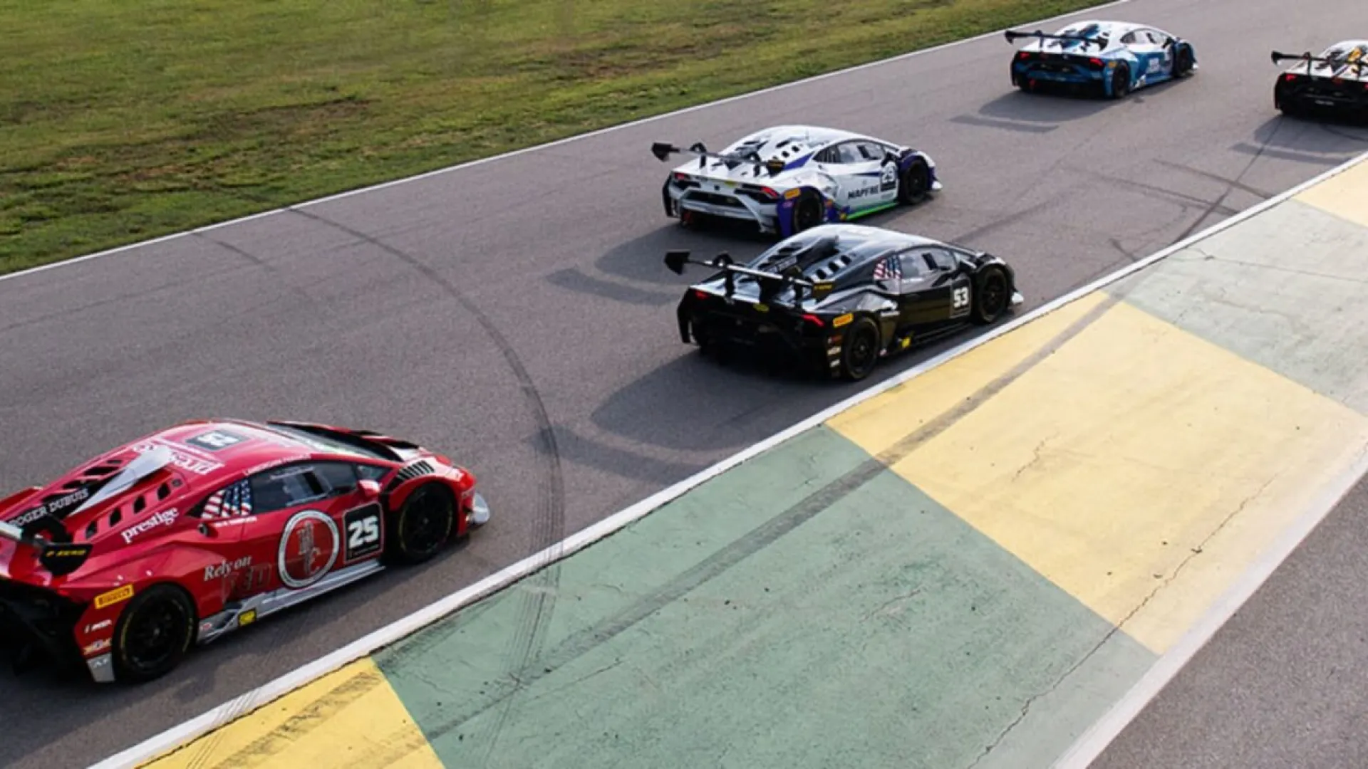 Race cars lined up on a track preparing for a high-speed motorsport event under clear daylight.