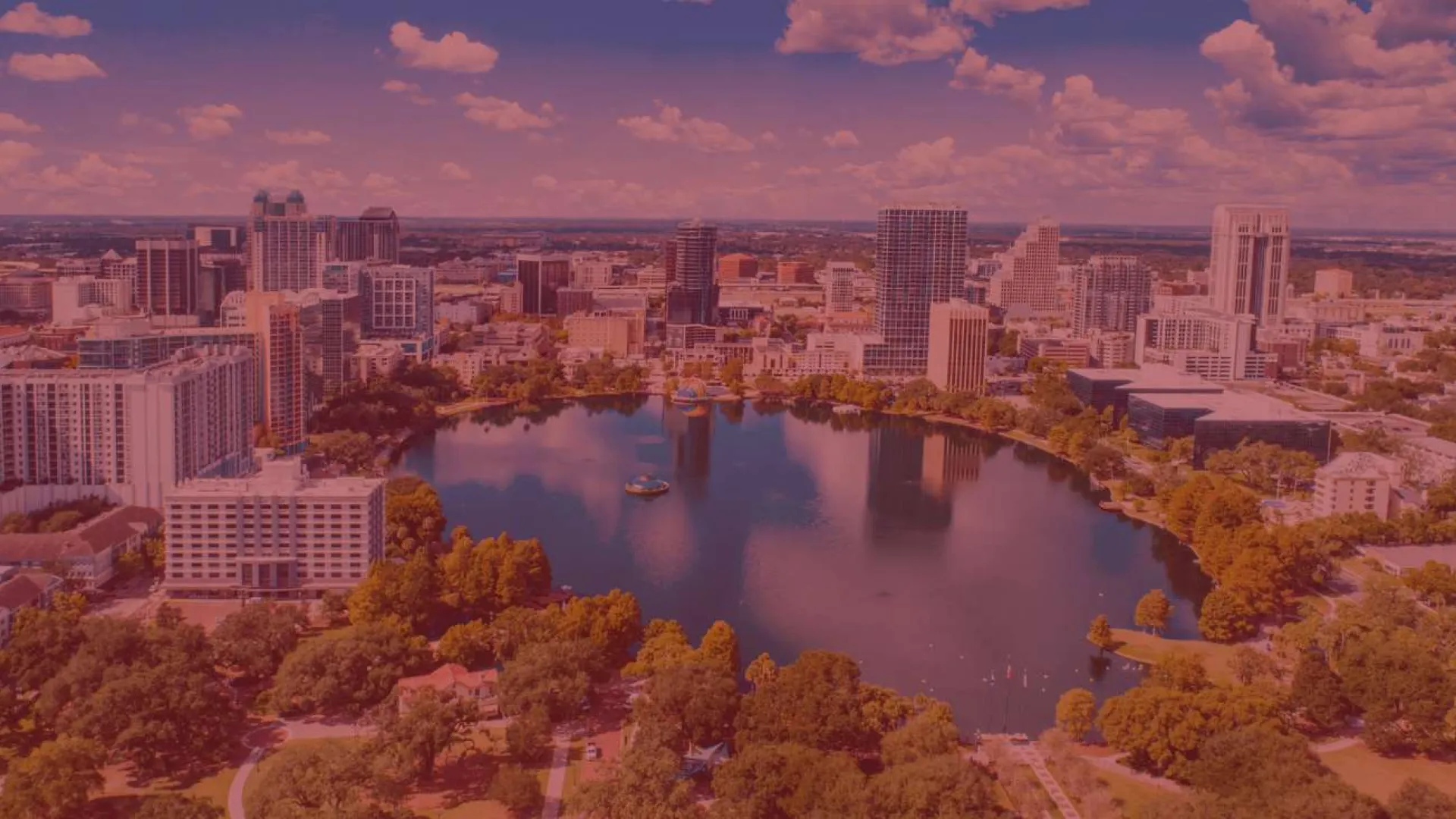 Aerial view of Orlando city skyline with lake and surrounding green parks under partly cloudy sky