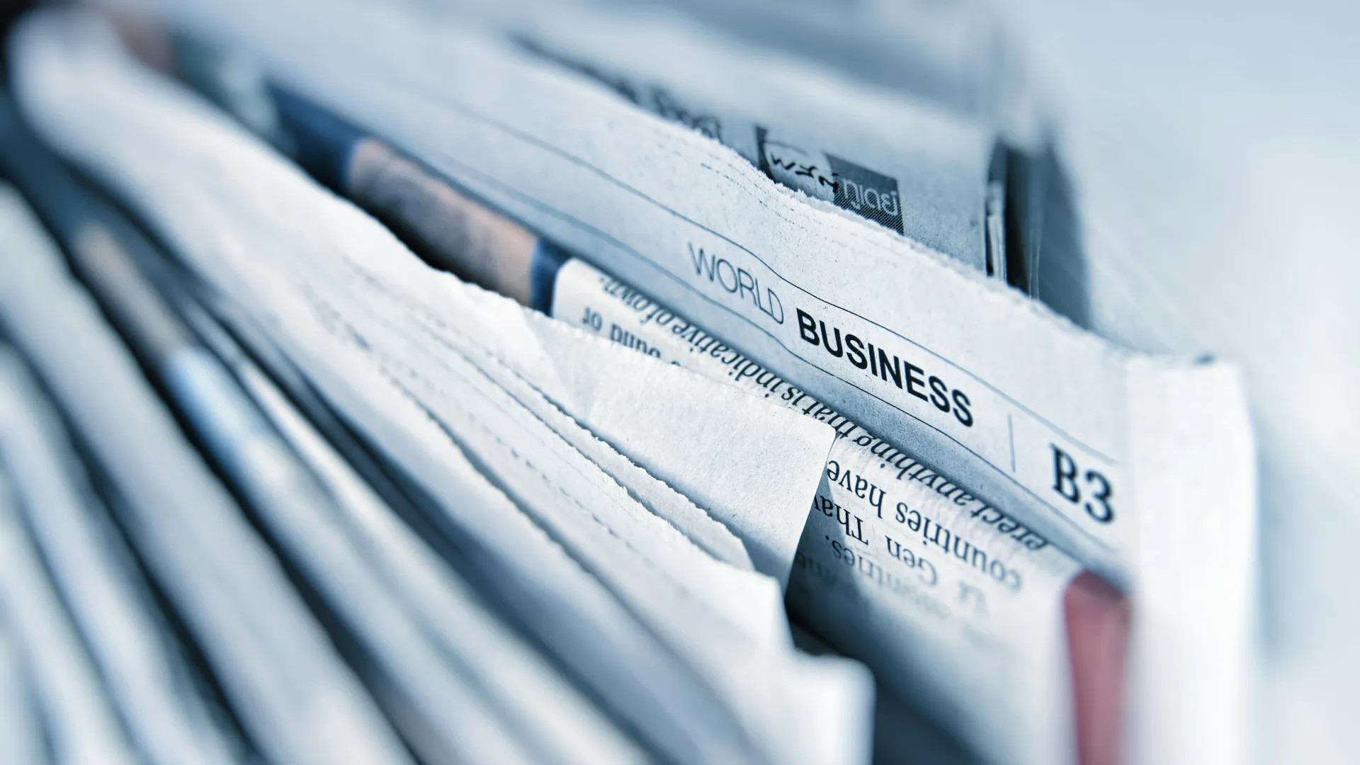 Close-up of folded business section newspapers stacked with visible headlines and articles.