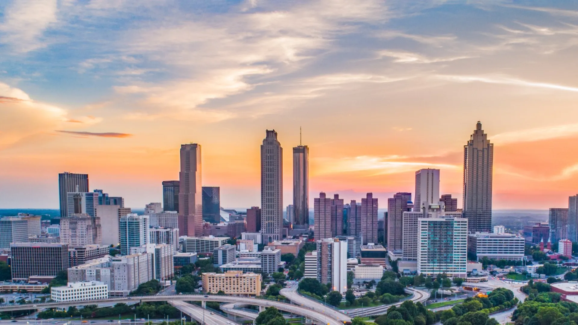 Sunset over Atlanta skyline with highways, residential areas, and skyscrapers under a colorful sky.