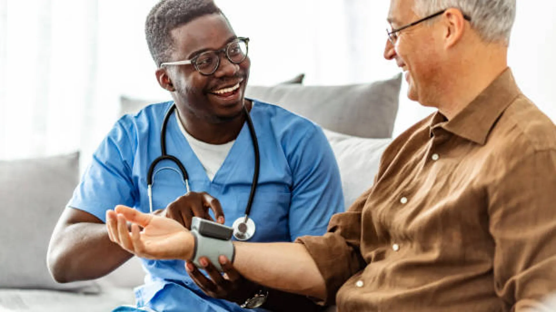 Health professional measuring blood pressure of an elderly man at home, ensuring wellness and care.