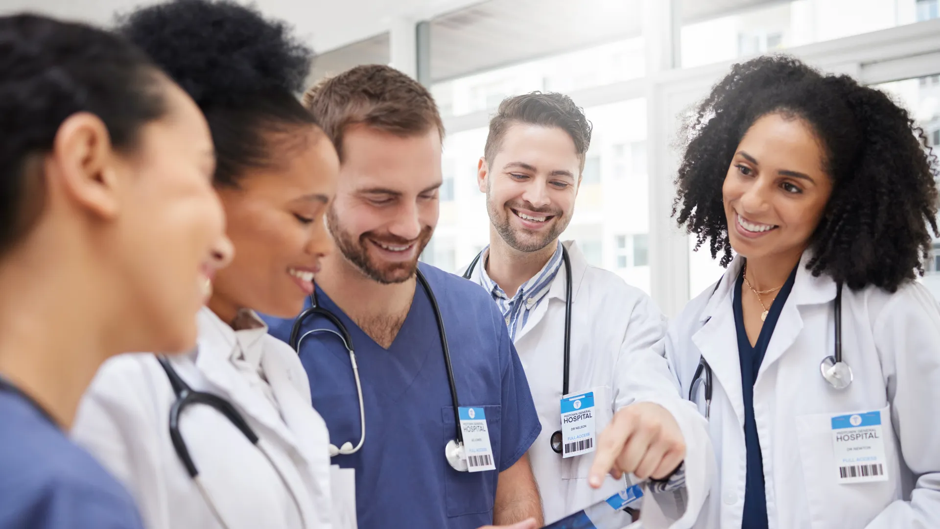 Diverse group of medical professionals reviewing patient data on a tablet in a bright hospital setting