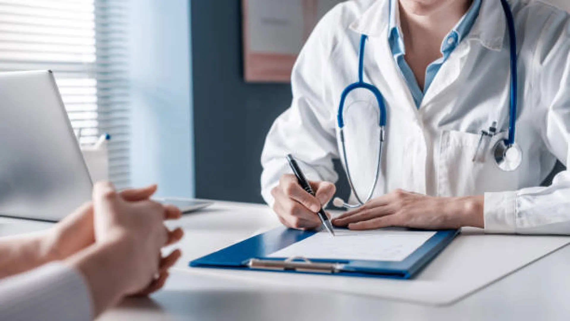 A healthcare professional taking notes during a patient consultation in a medical office.