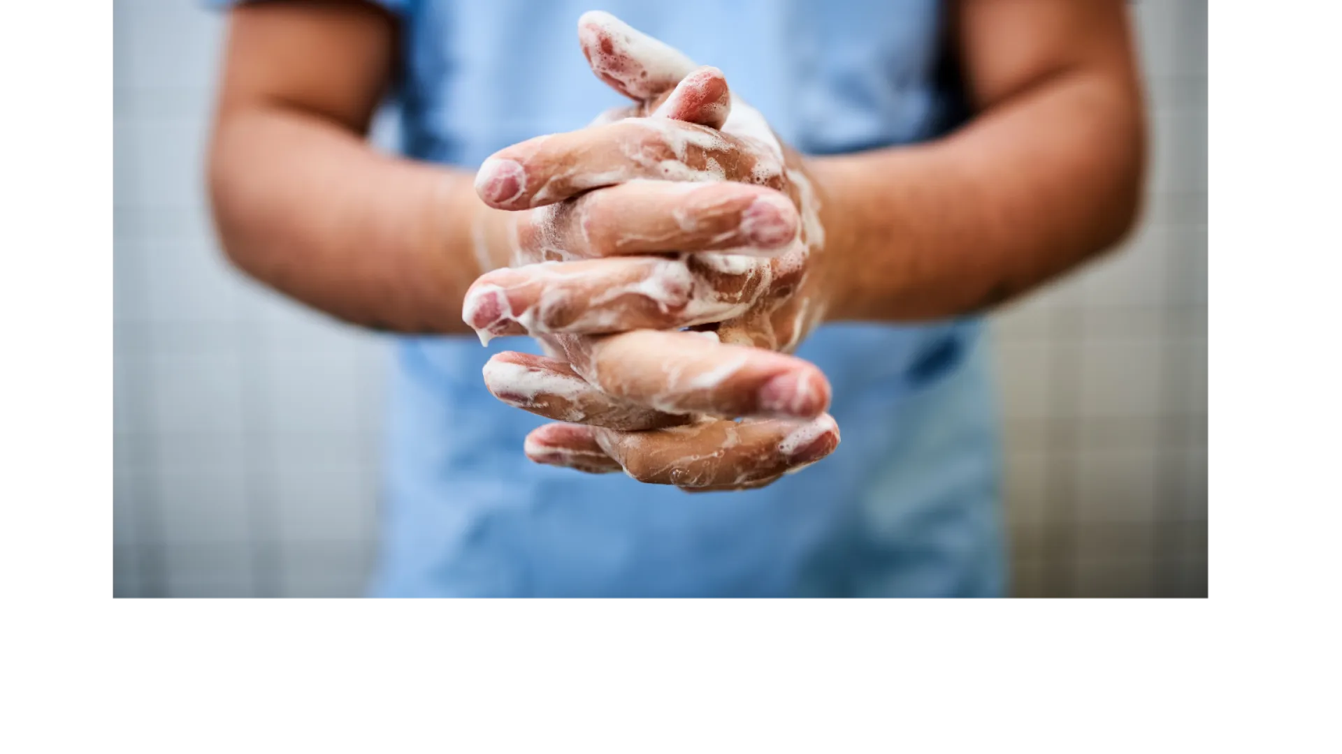 Person in blue scrubs washing hands with soap to maintain hygiene and prevent infection.