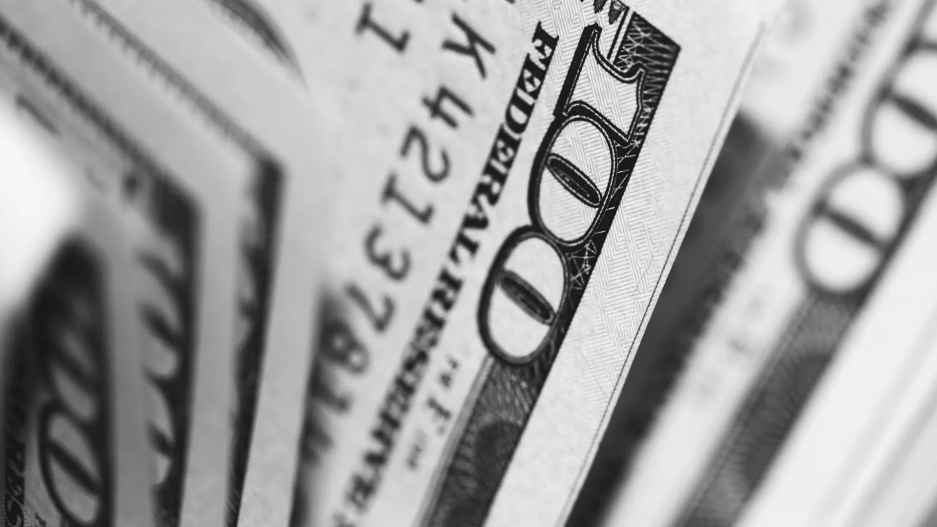 Close-up of multiple US 100-dollar bills in black and white showing detailed security features.