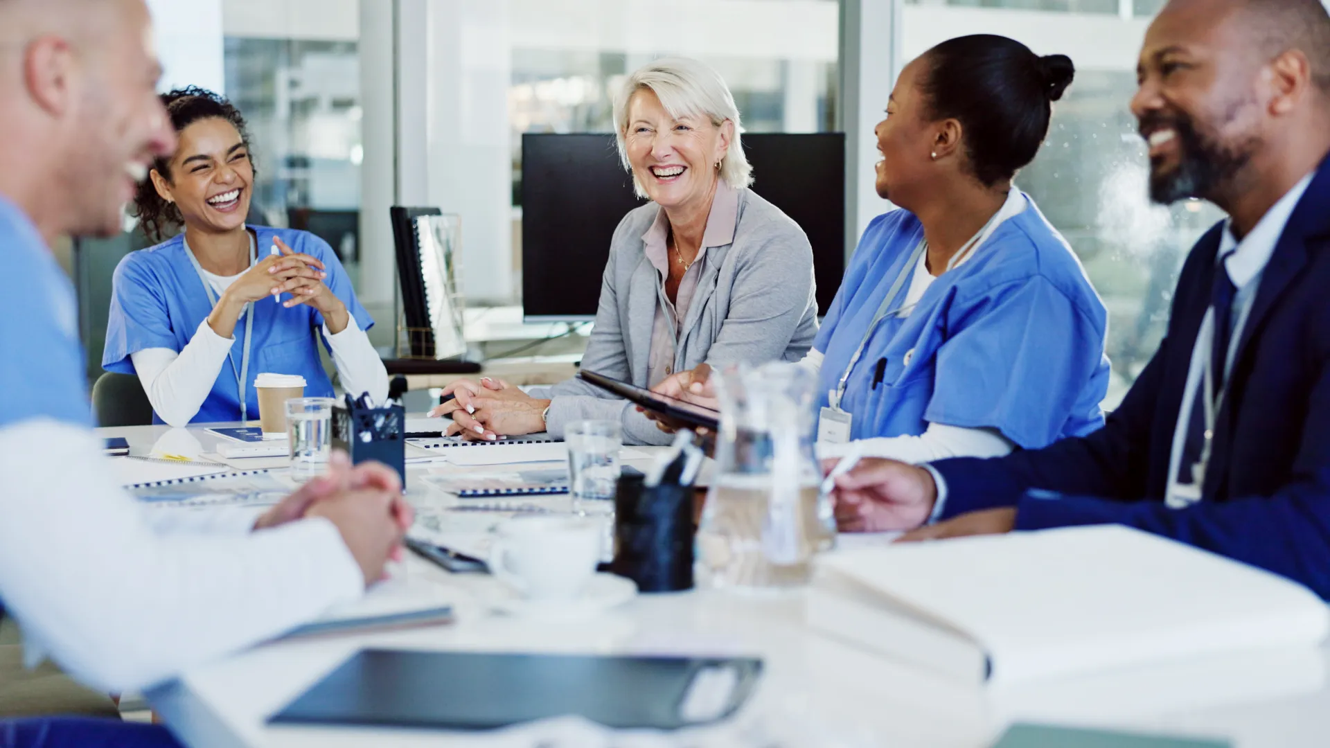 Diverse medical team and business professional smiling and discussing around a table in a bright office meeting.