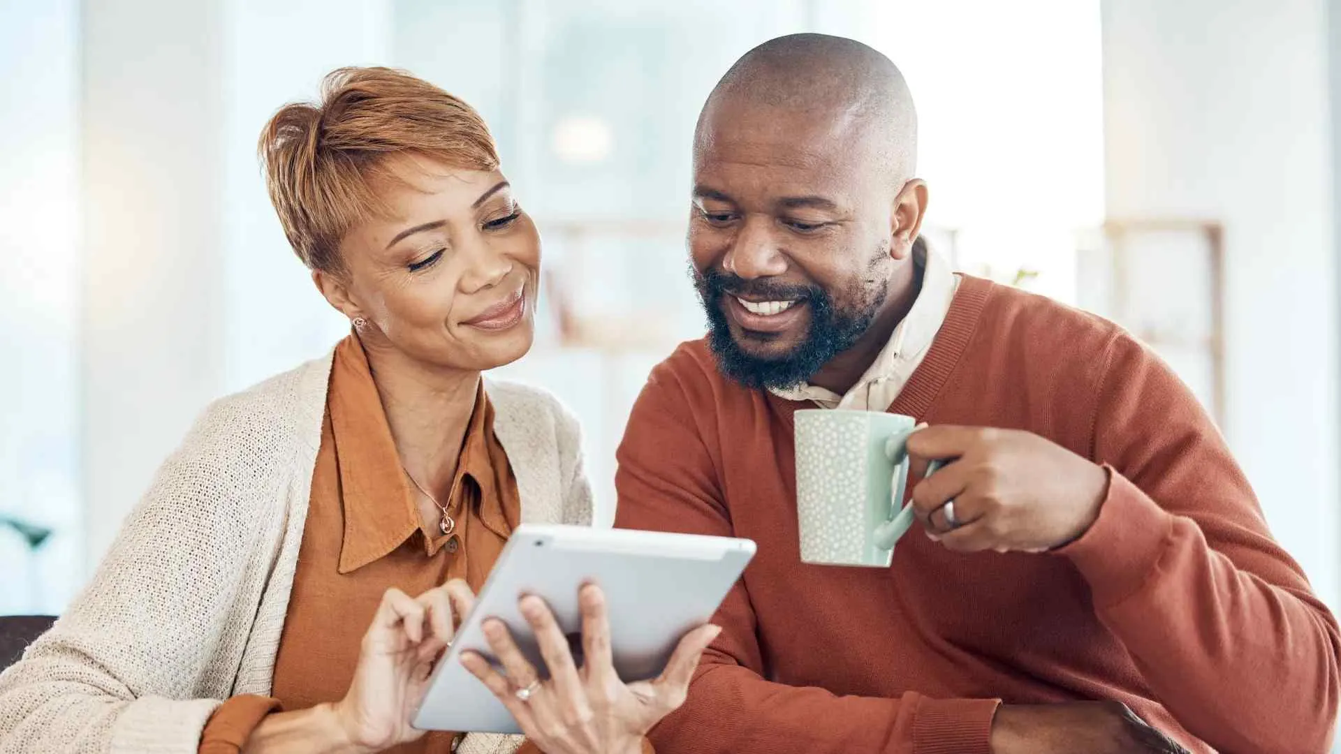 Smiling couple using a digital tablet and enjoying coffee together in a bright modern home.