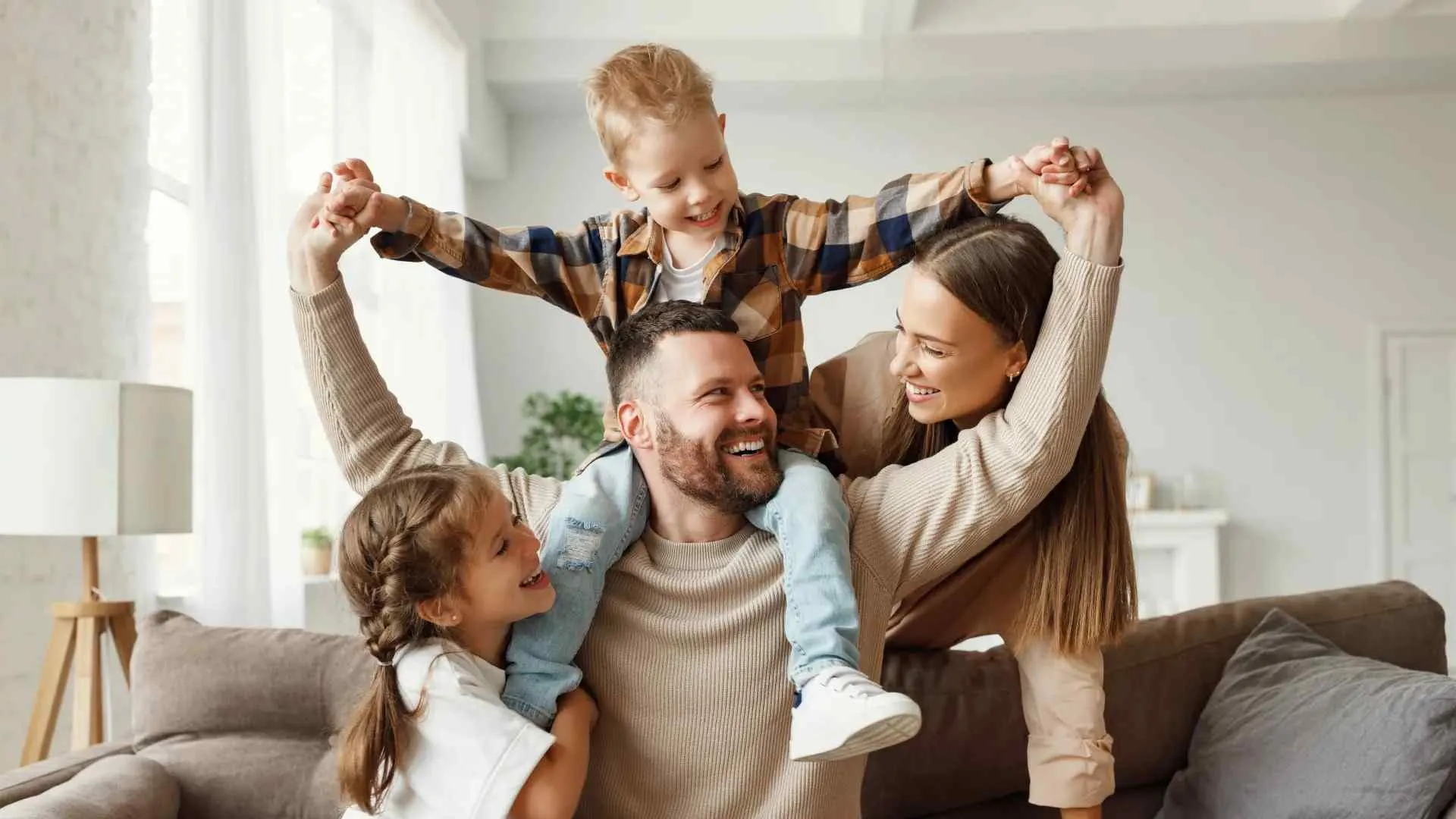 Happy family of four playing together in a bright living room, smiling and bonding joyfully.