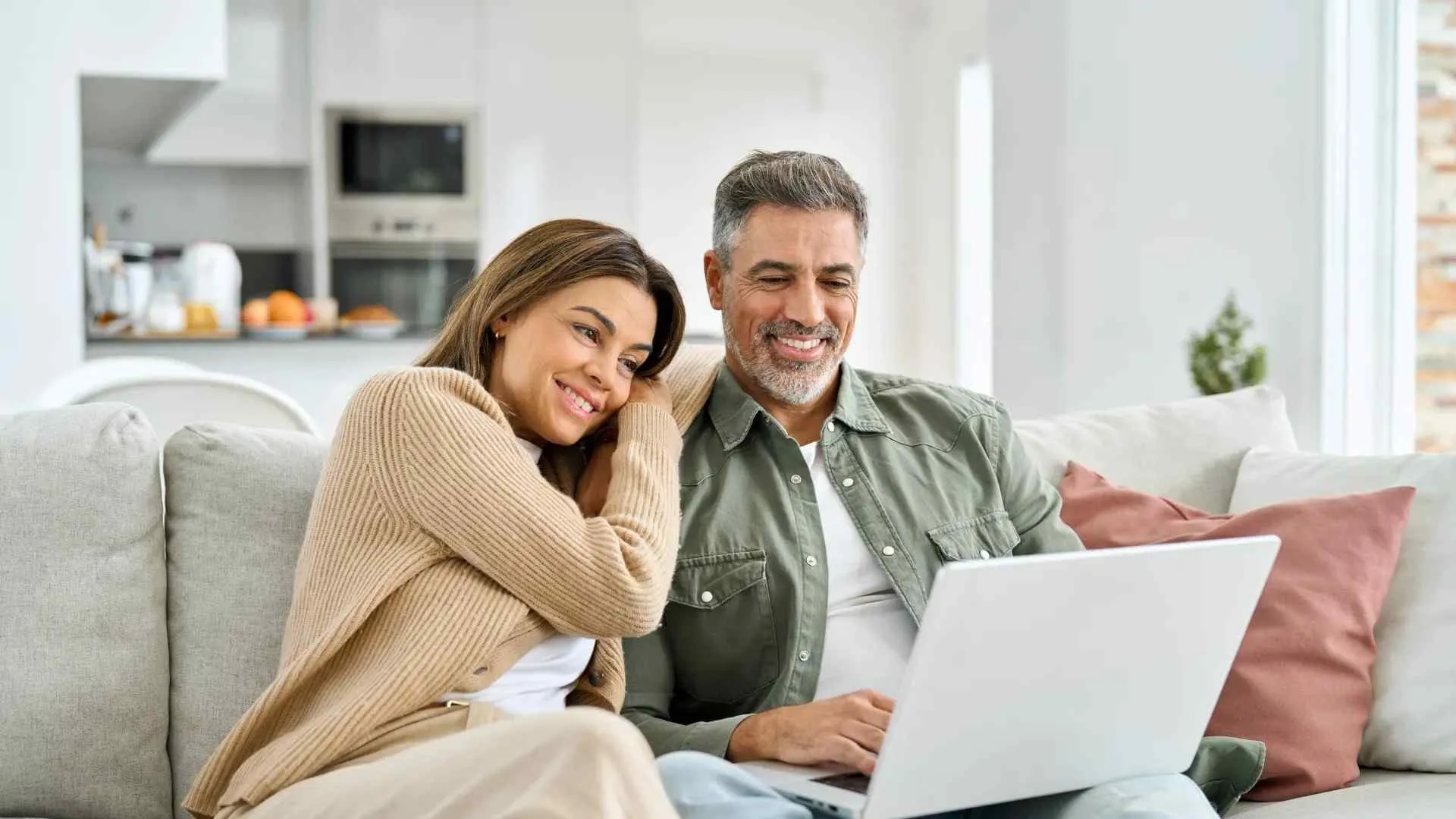 Smiling couple sitting on couch using laptop together in cozy living room setting