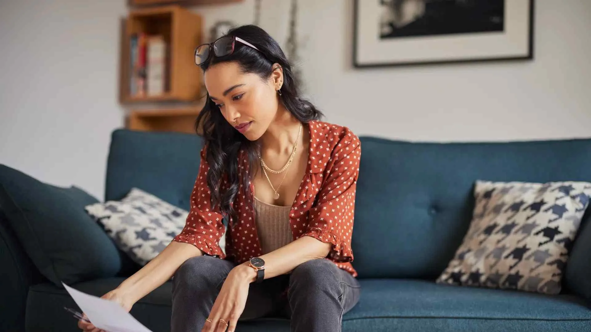 Young woman in casual outfit sitting on blue couch reading documents attentively in cozy living room.