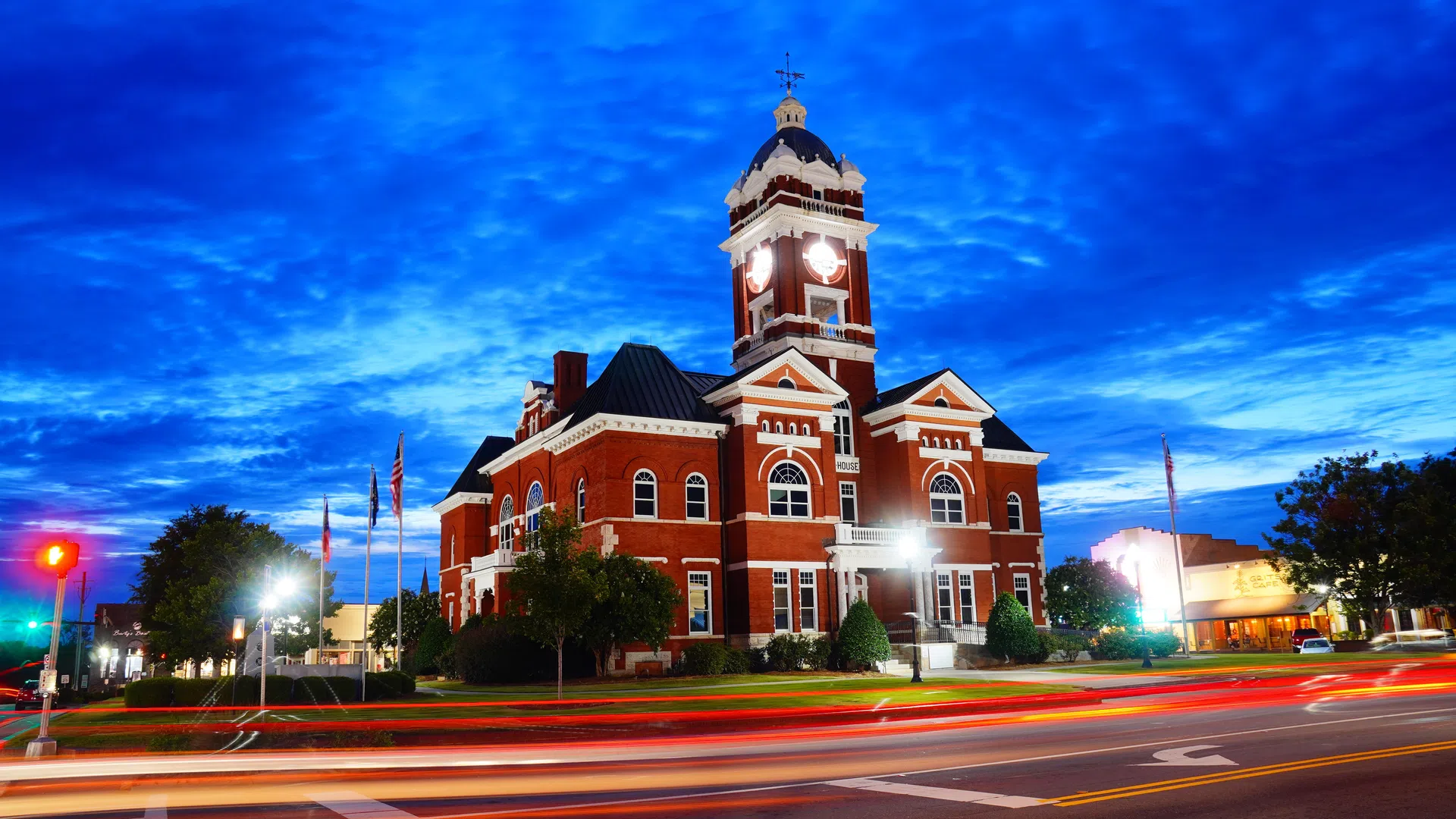 Historic red brick courthouse with clock tower illuminated at dusk and light trails from passing traffic.