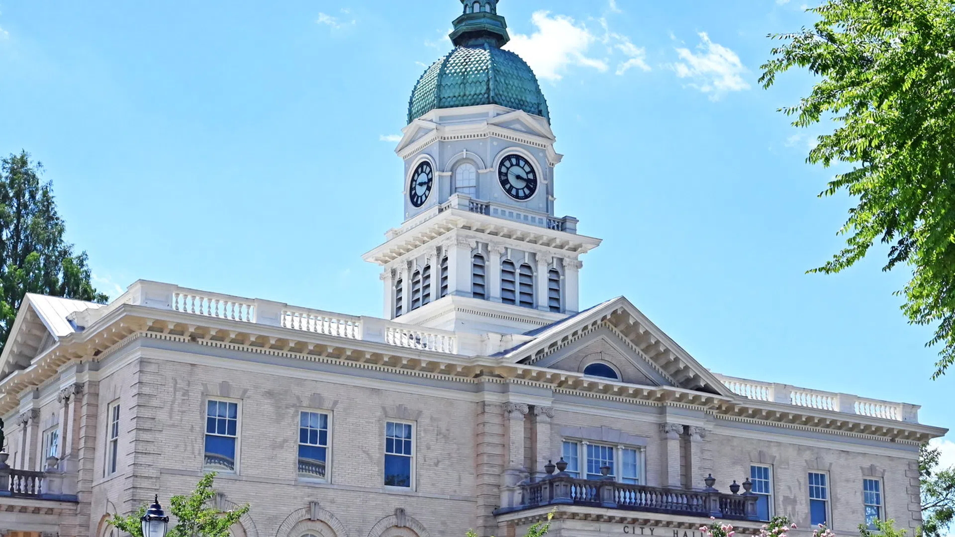 Historic courthouse building with clock tower under clear blue sky and surrounding green trees.