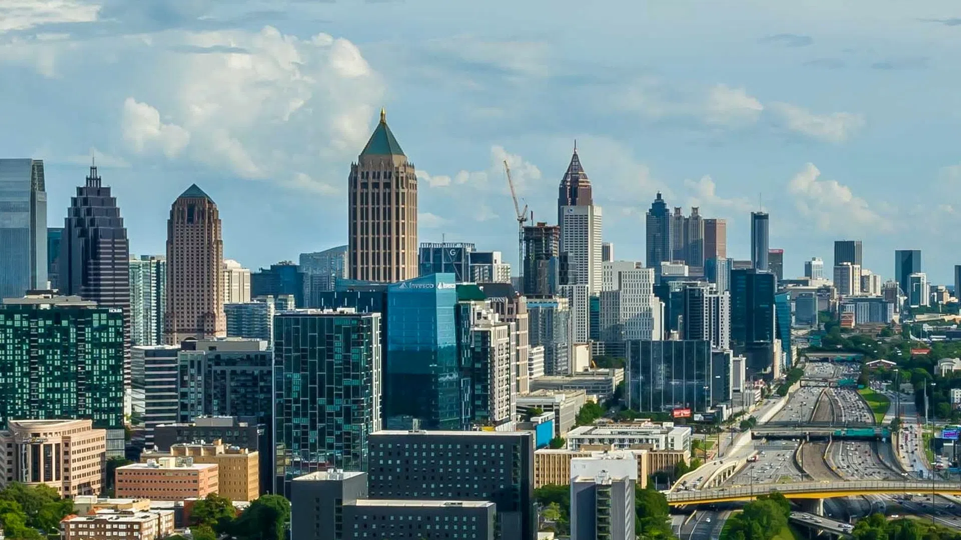Skyline of a modern city with high-rise buildings and busy highways under a partly cloudy sky.