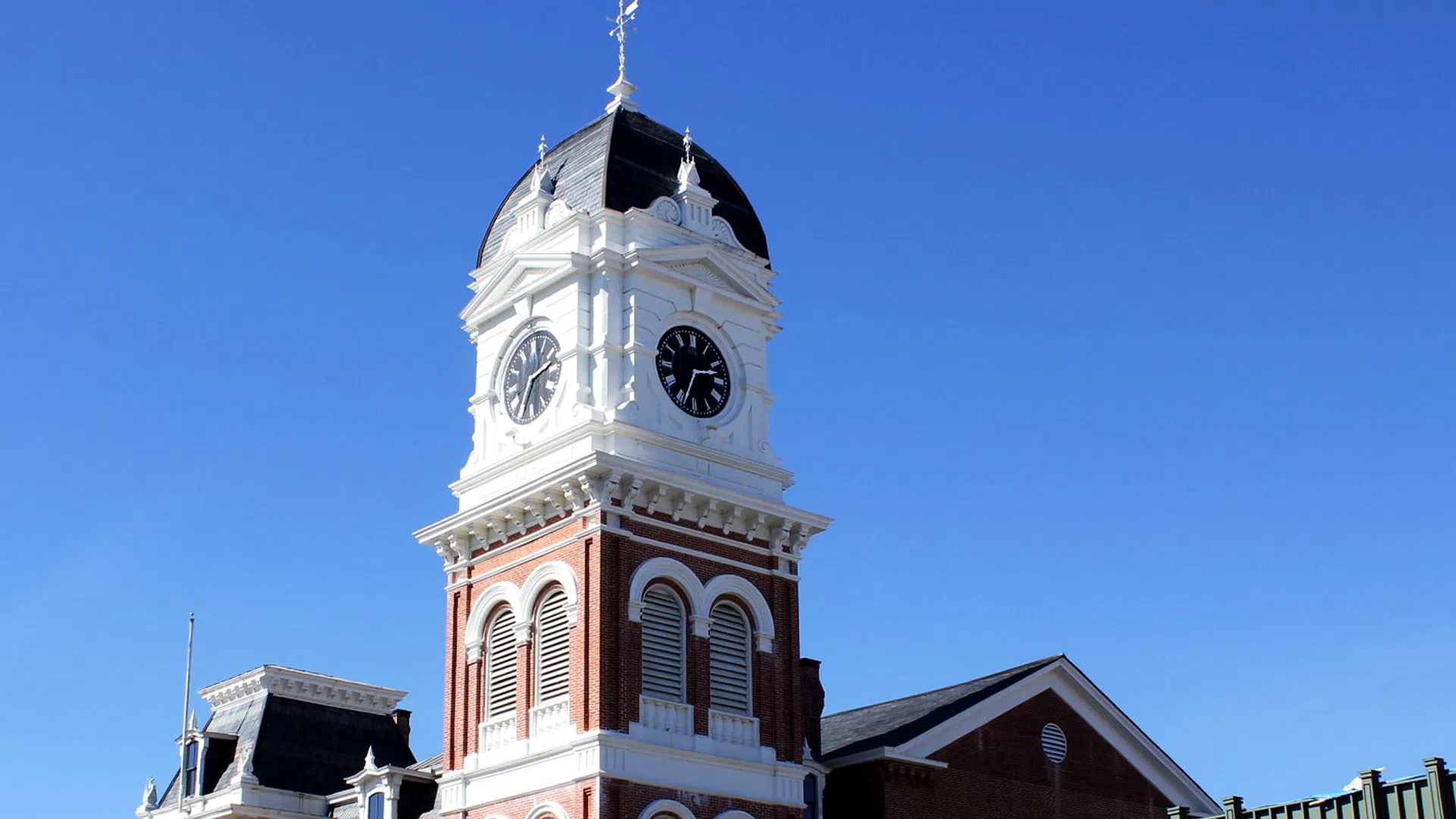 Historic clock tower with white and red brick facade against a clear blue sky on a sunny day