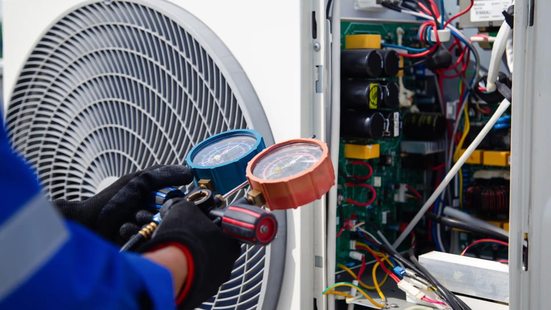 Technician in gloves using gauges to check and repair an air conditioning unit's electrical components.