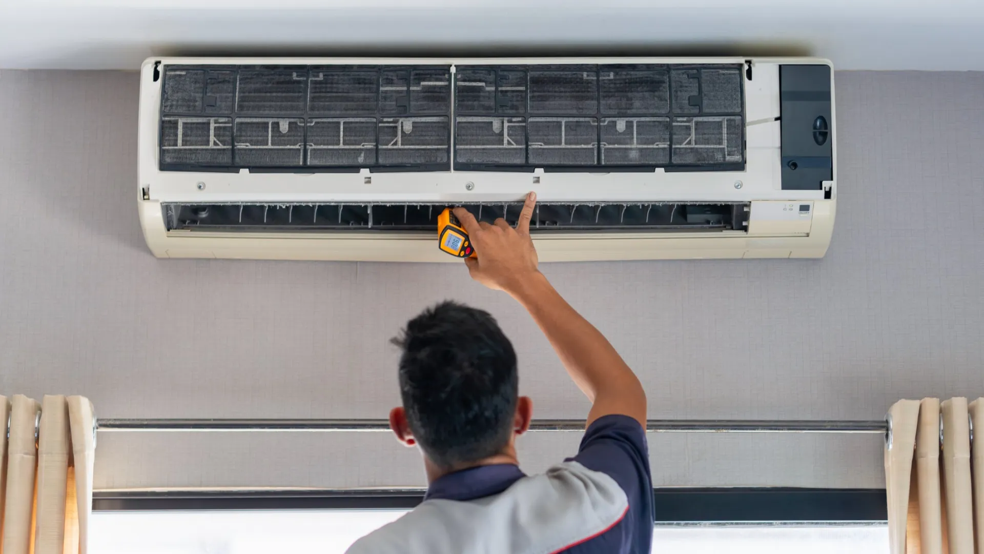 Technician inspecting and repairing a wall-mounted air conditioner with a handheld device indoors.