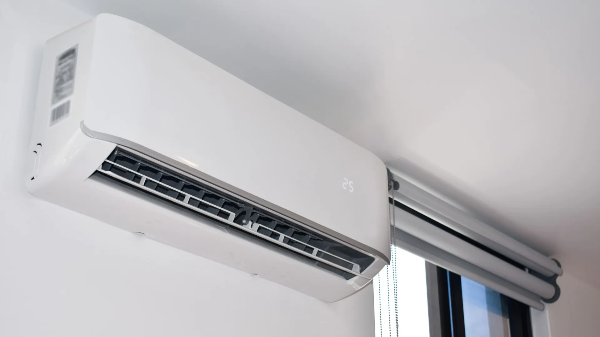 Modern white wall-mounted air conditioner unit displaying temperature 25 installed near window.