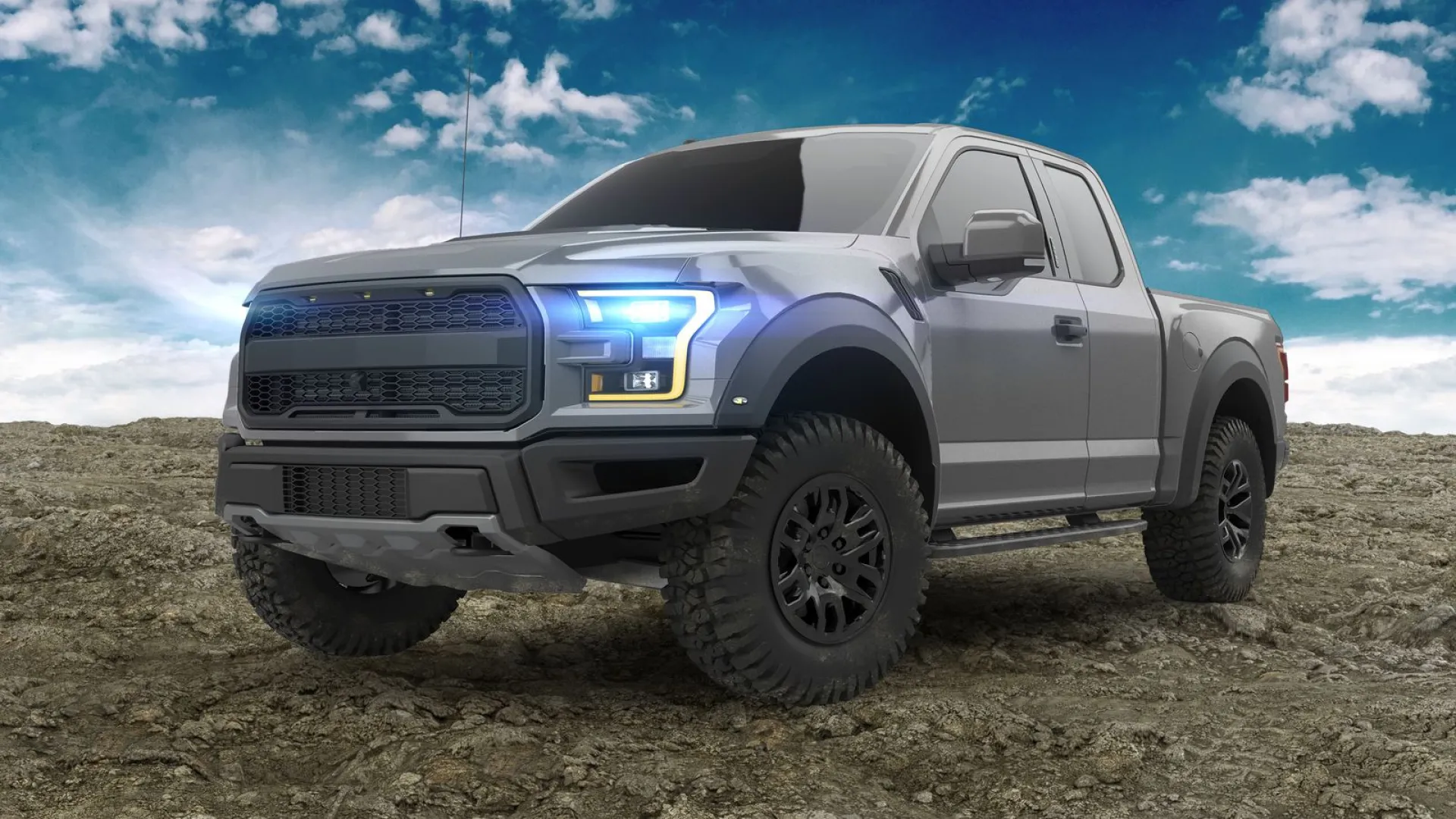 Gray off-road pickup truck with large tires on rugged terrain under a cloudy blue sky.