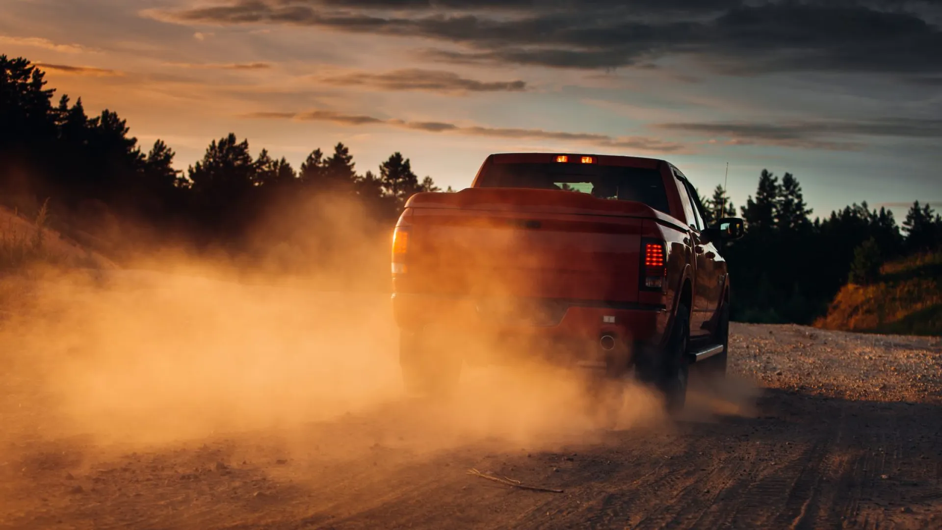 a car on a dirt road with a large fire in the back