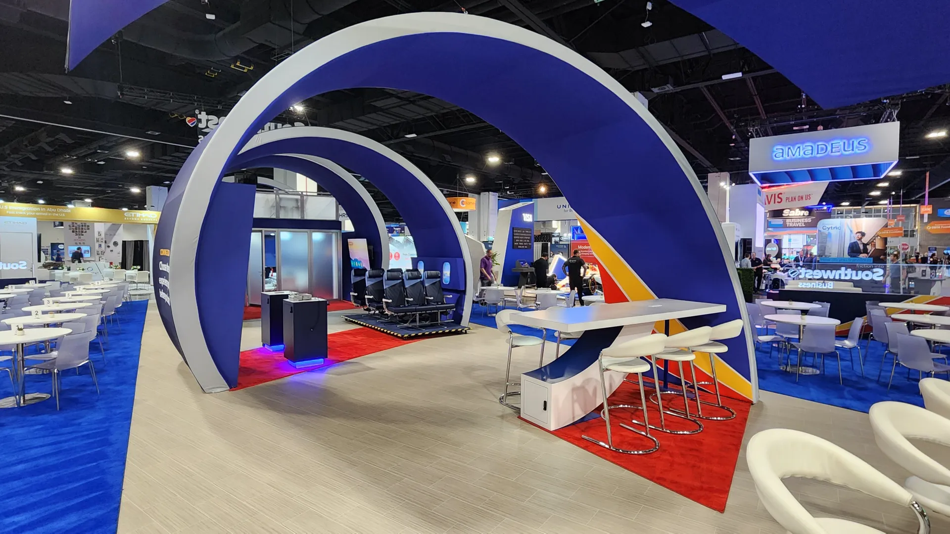 Modern conference booth with blue and white arches, seating areas, and a vibrant carpeted floor at trade show.