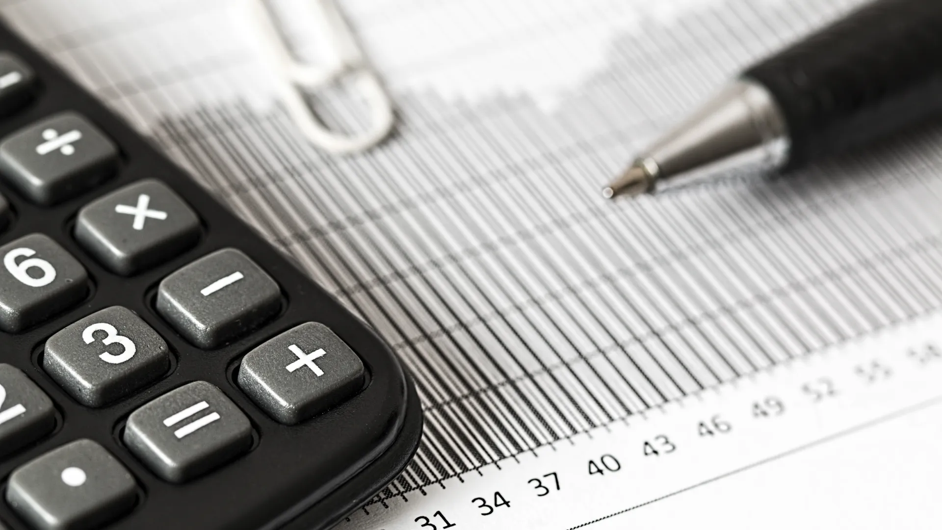 Calculator, pen, and paperclip on financial document with numerical data and grid lines in close-up.