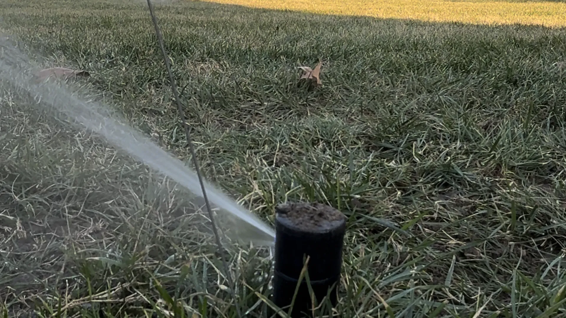 Sprinkler system spraying water onto grass, with a service truck visible in the background.