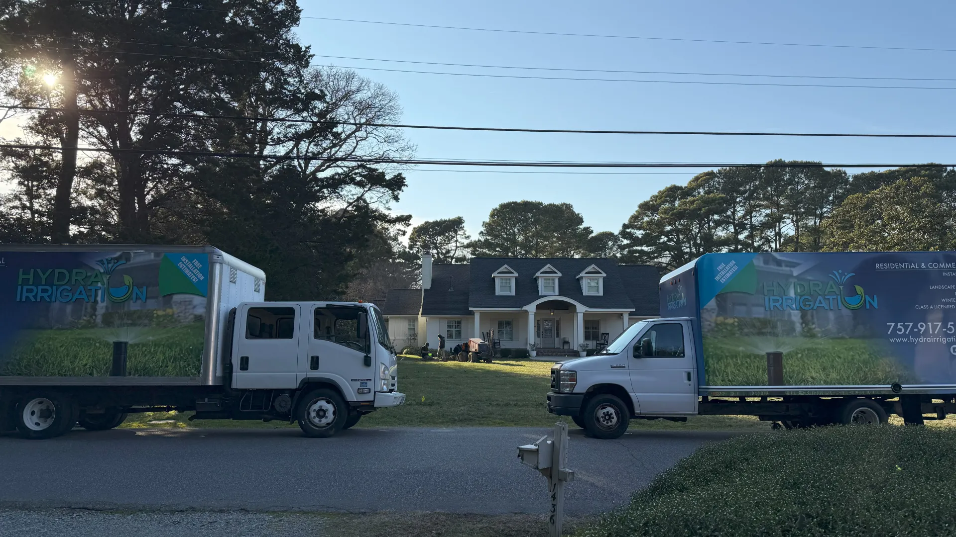 Two irrigation service trucks parked outside a home under clear blue skies.