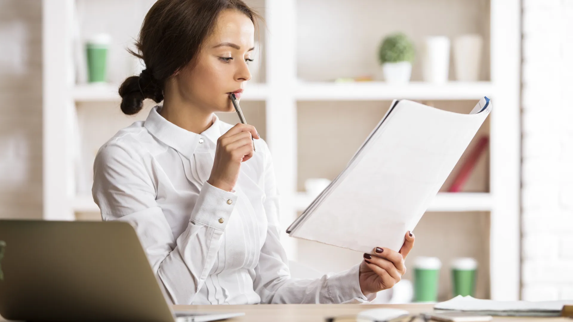 a person holding a pen and looking at a laptop