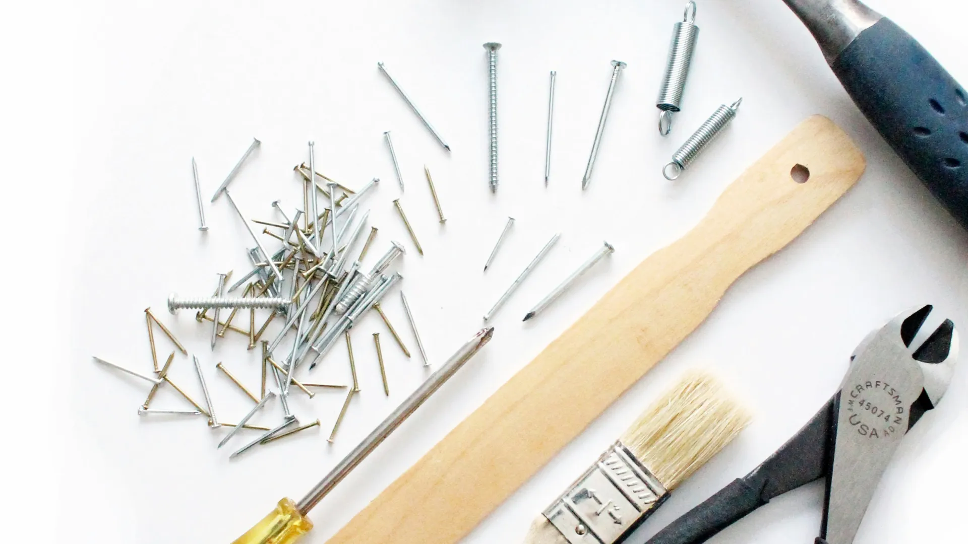 Hammer, screwdriver, pliers, paintbrush, wooden stick, springs, and nails on white background.