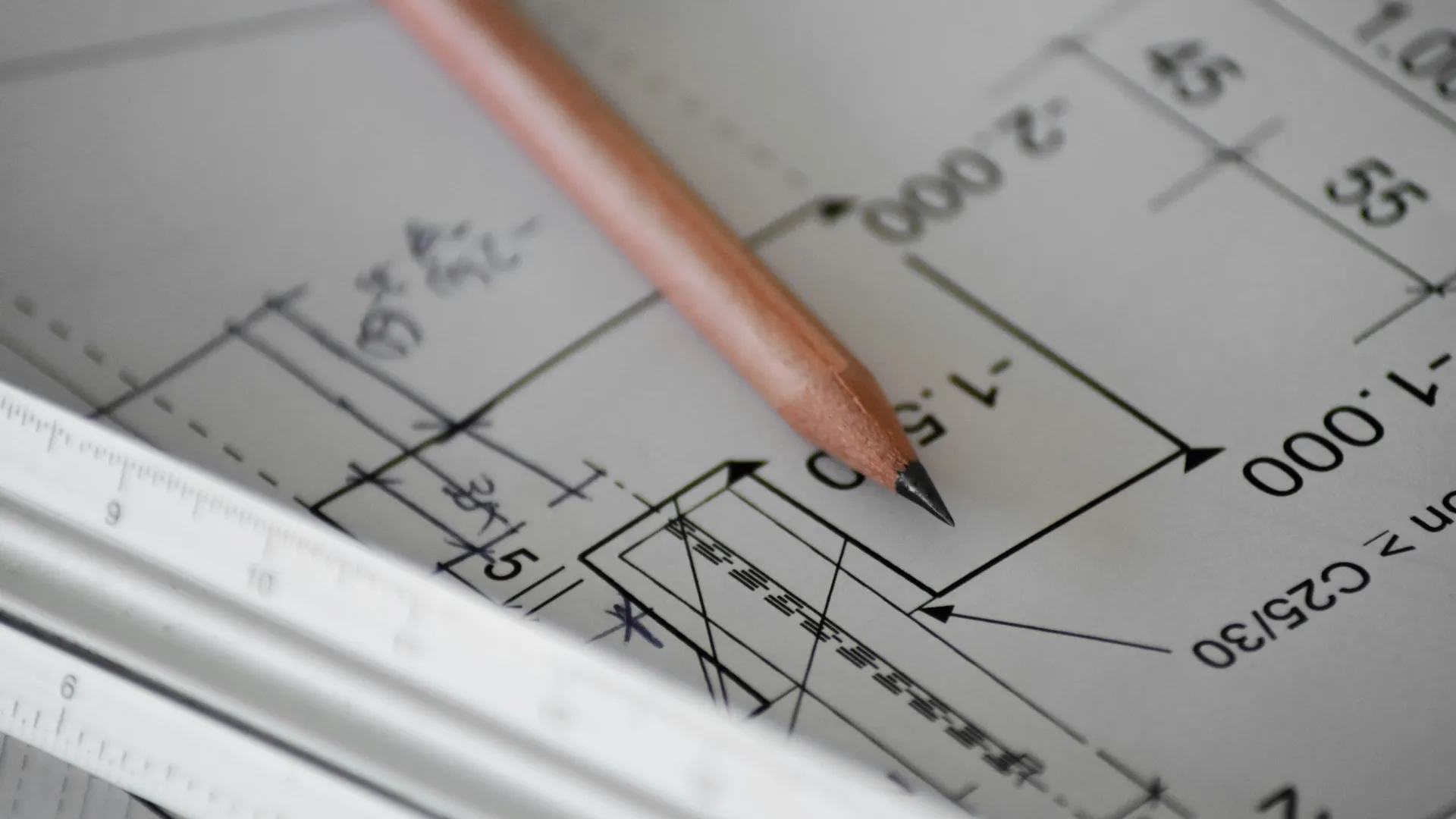 Close-up of architectural blueprint with pencil and scale ruler highlighting measurements and design details.