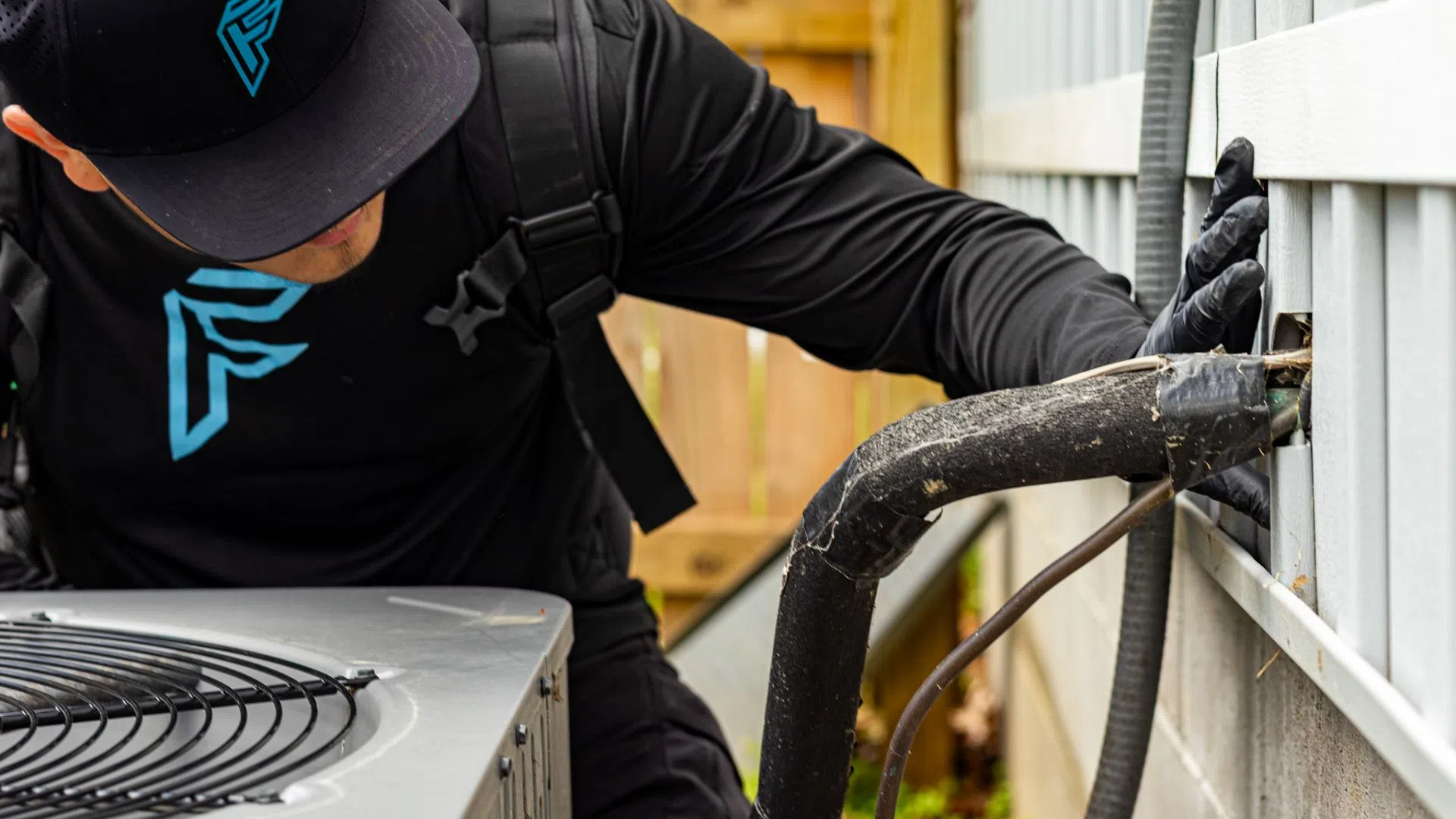 Technician inspecting and repairing an outdoor air conditioning unit with insulated pipes connected to the house.