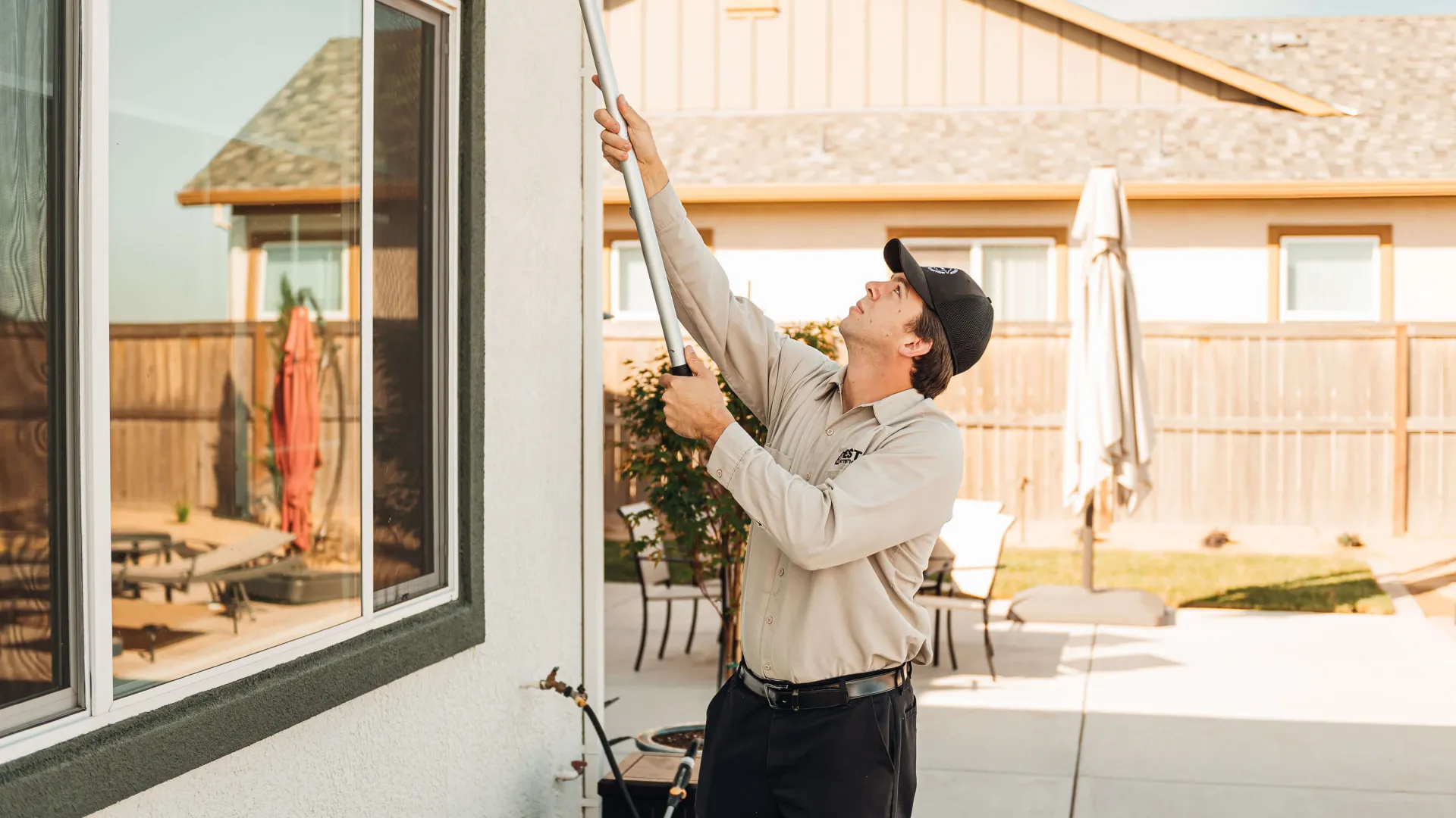 Technician in uniform using a pole to clean or inspect a window outside a residential house on a sunny day