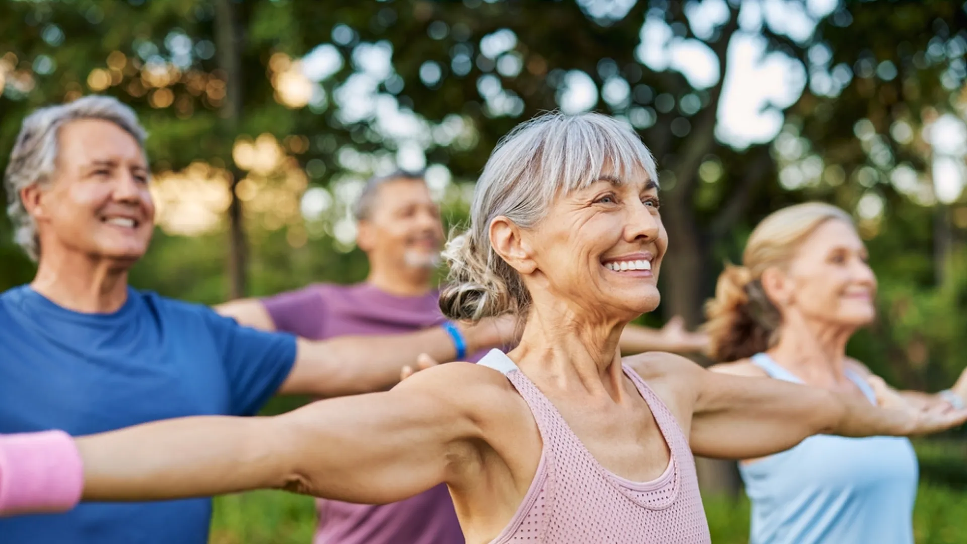 Group of smiling seniors doing outdoor stretching exercises in a park on a sunny day