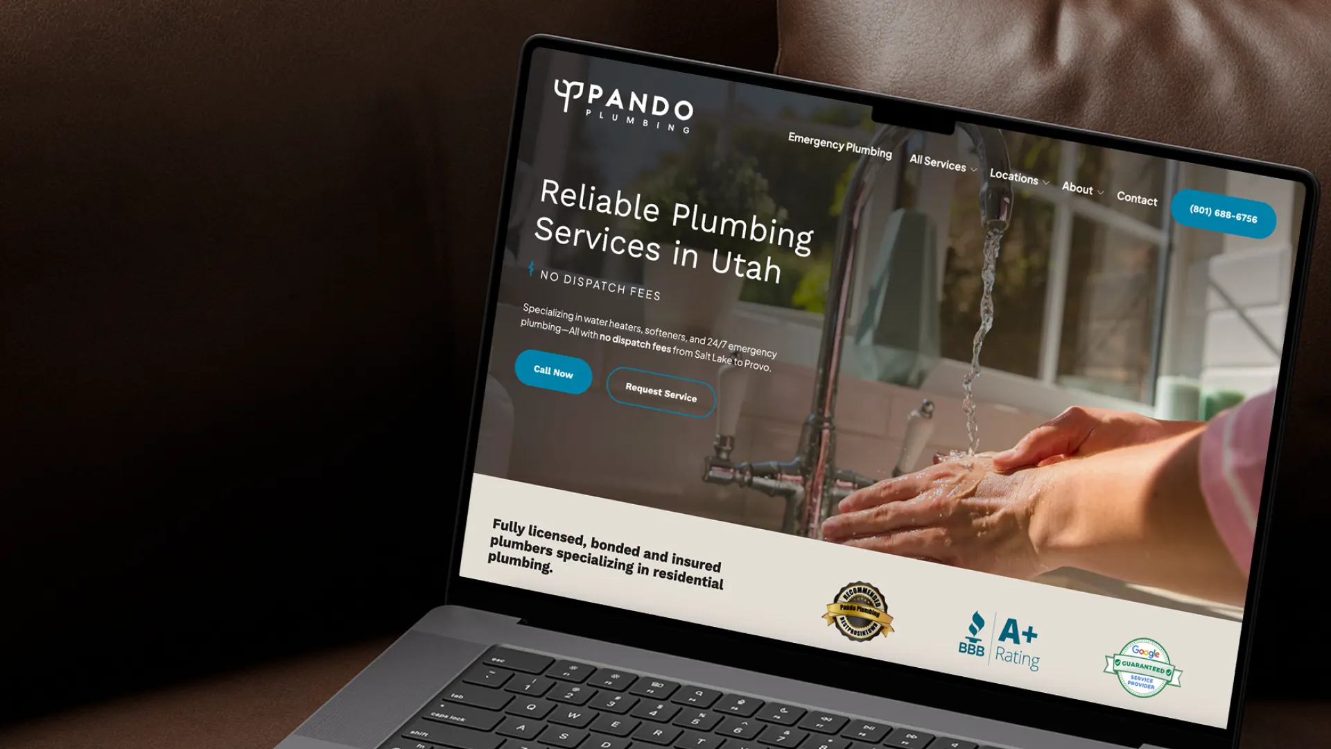 Laptop showing Upando Plumbing website with hands washing under a running faucet in the background
