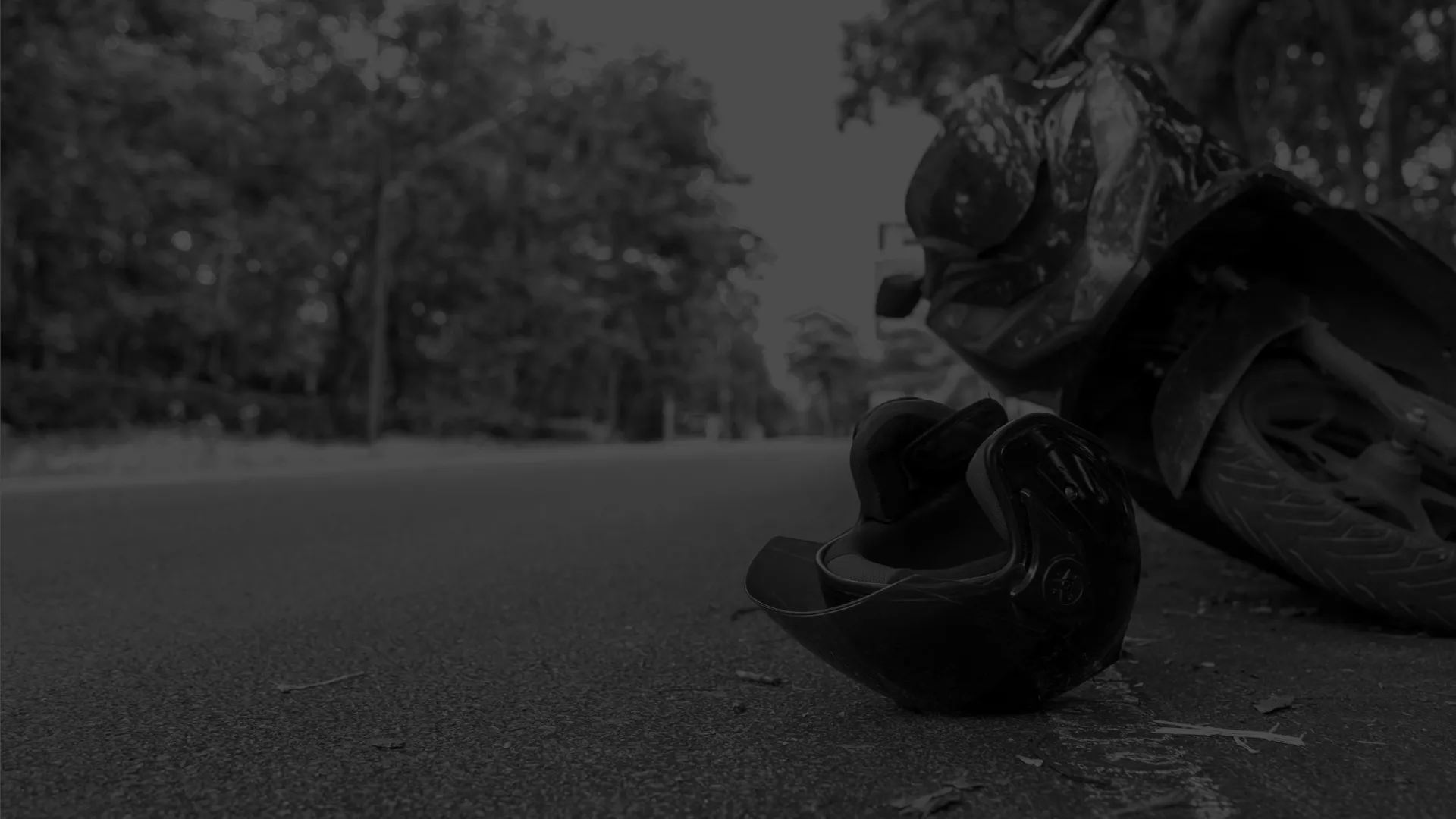 Motorcycle helmet lying on road beside a parked motorcycle with trees in the background under daylight.