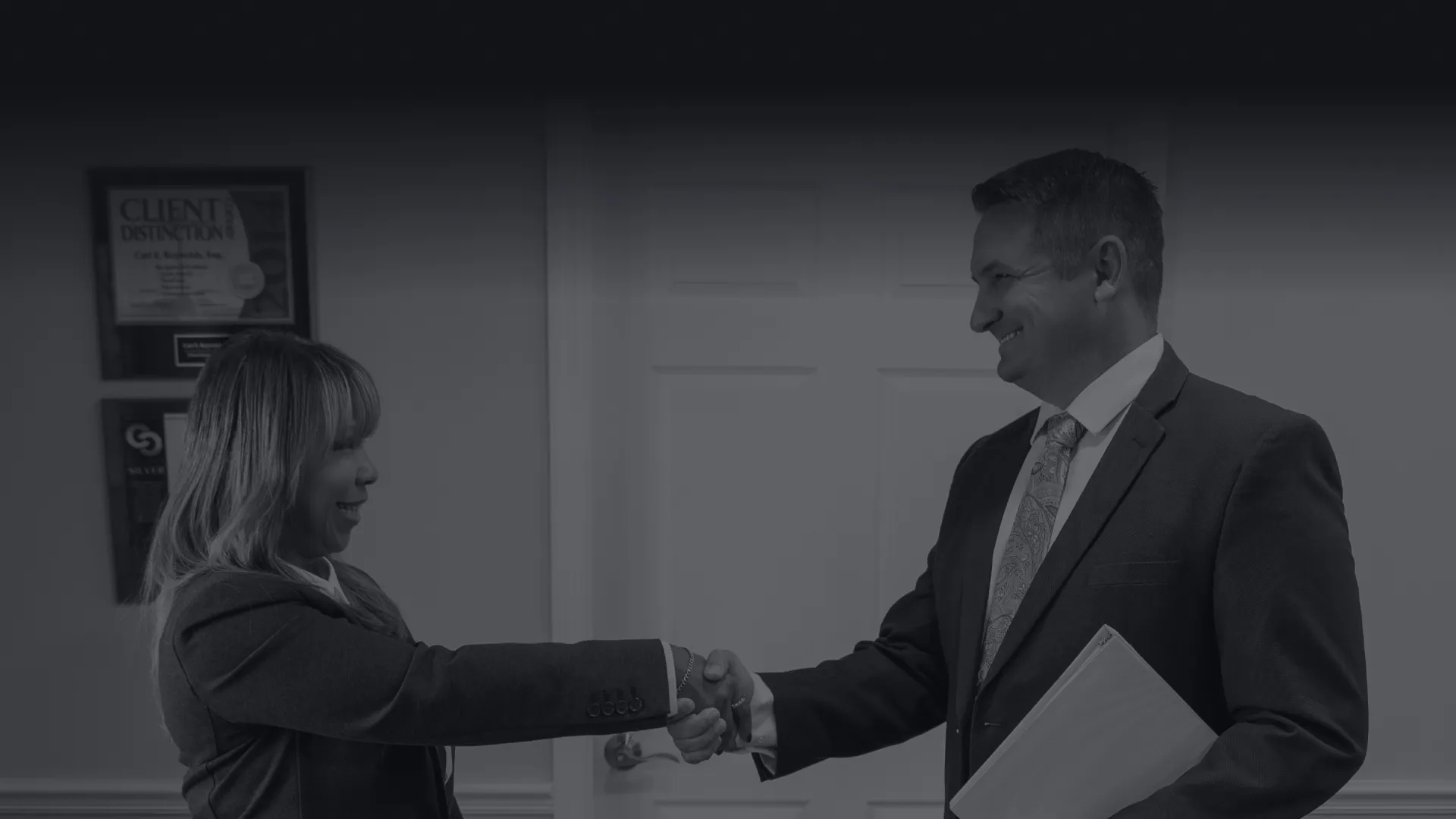 Two business professionals shaking hands in an office setting, symbolizing agreement and partnership.