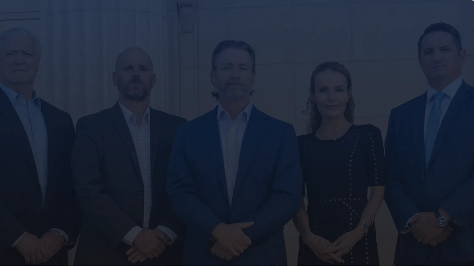 Five business professionals standing in formal attire against a marble wall, posing confidently.