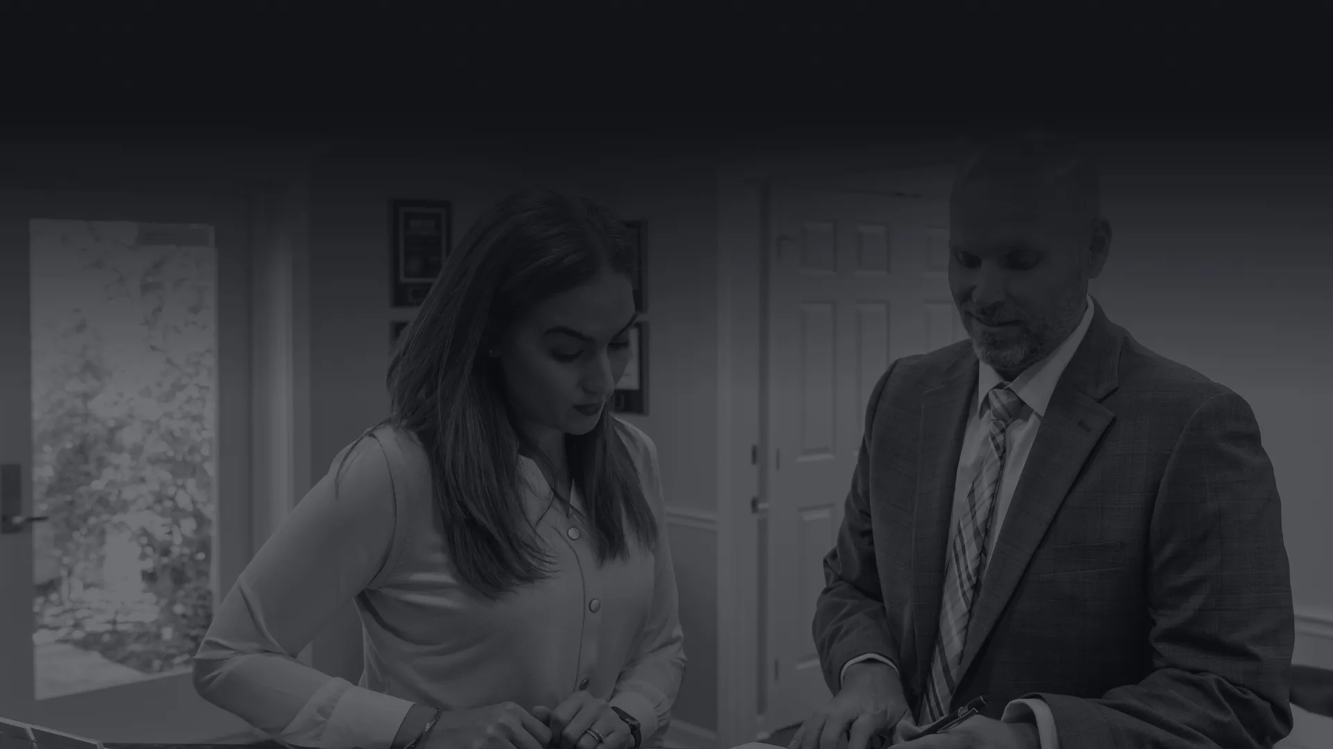 Man in suit explaining documents to woman at office reception desk in professional setting