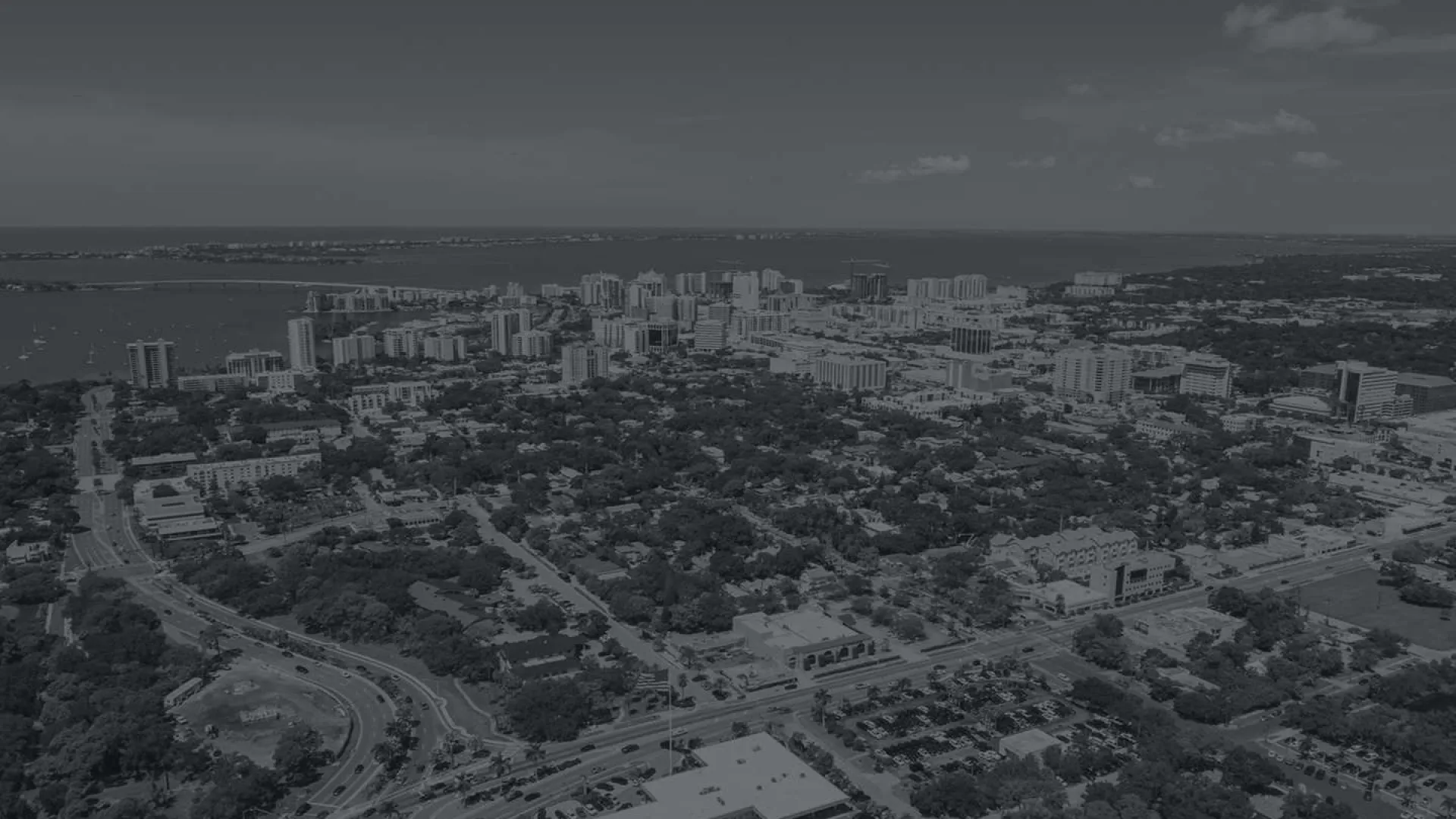 Aerial view of a coastal city with high-rise buildings, residential neighborhoods, and visible waterfront under a clear sky.