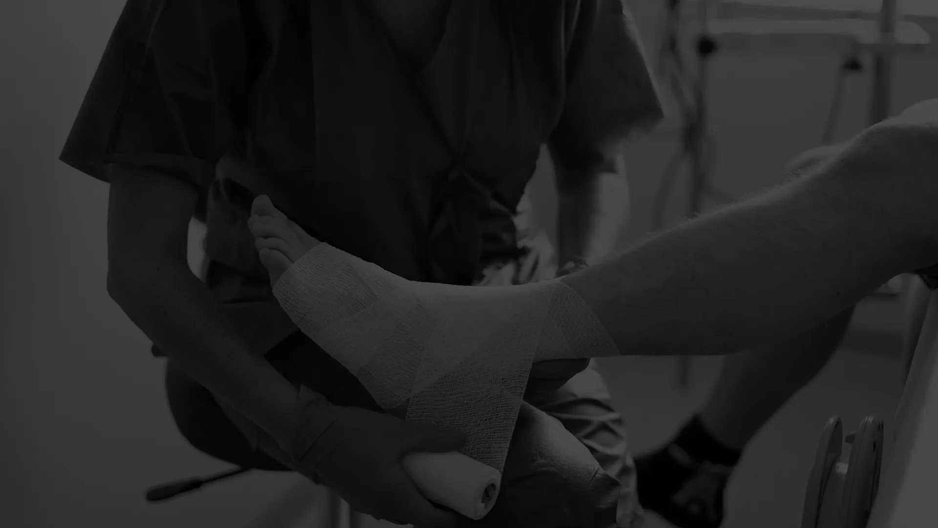 Healthcare professional wrapping a patient's ankle with a bandage in a medical setting.