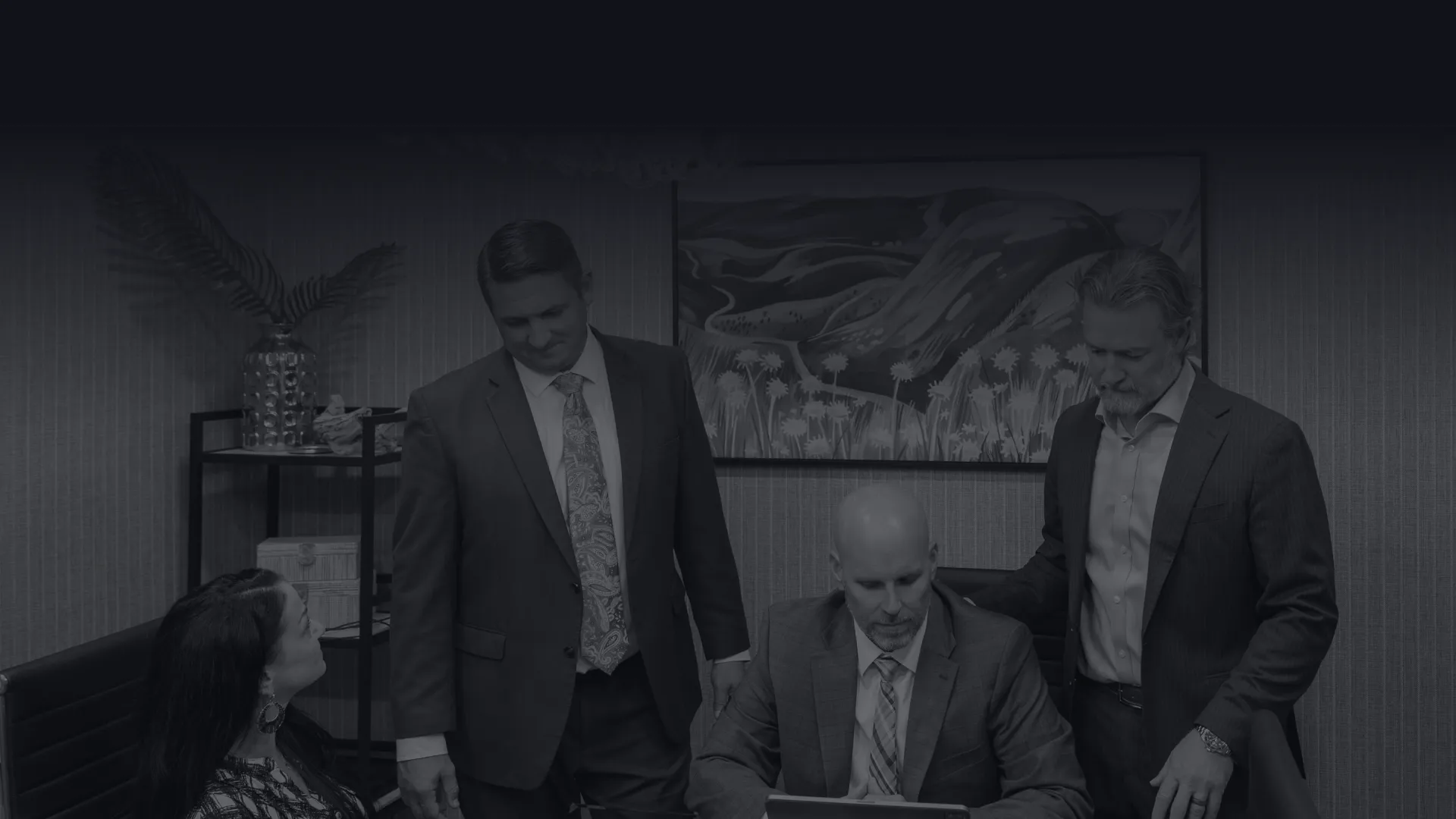 Four business professionals in suits collaborating around a glass table in a modern office setting.